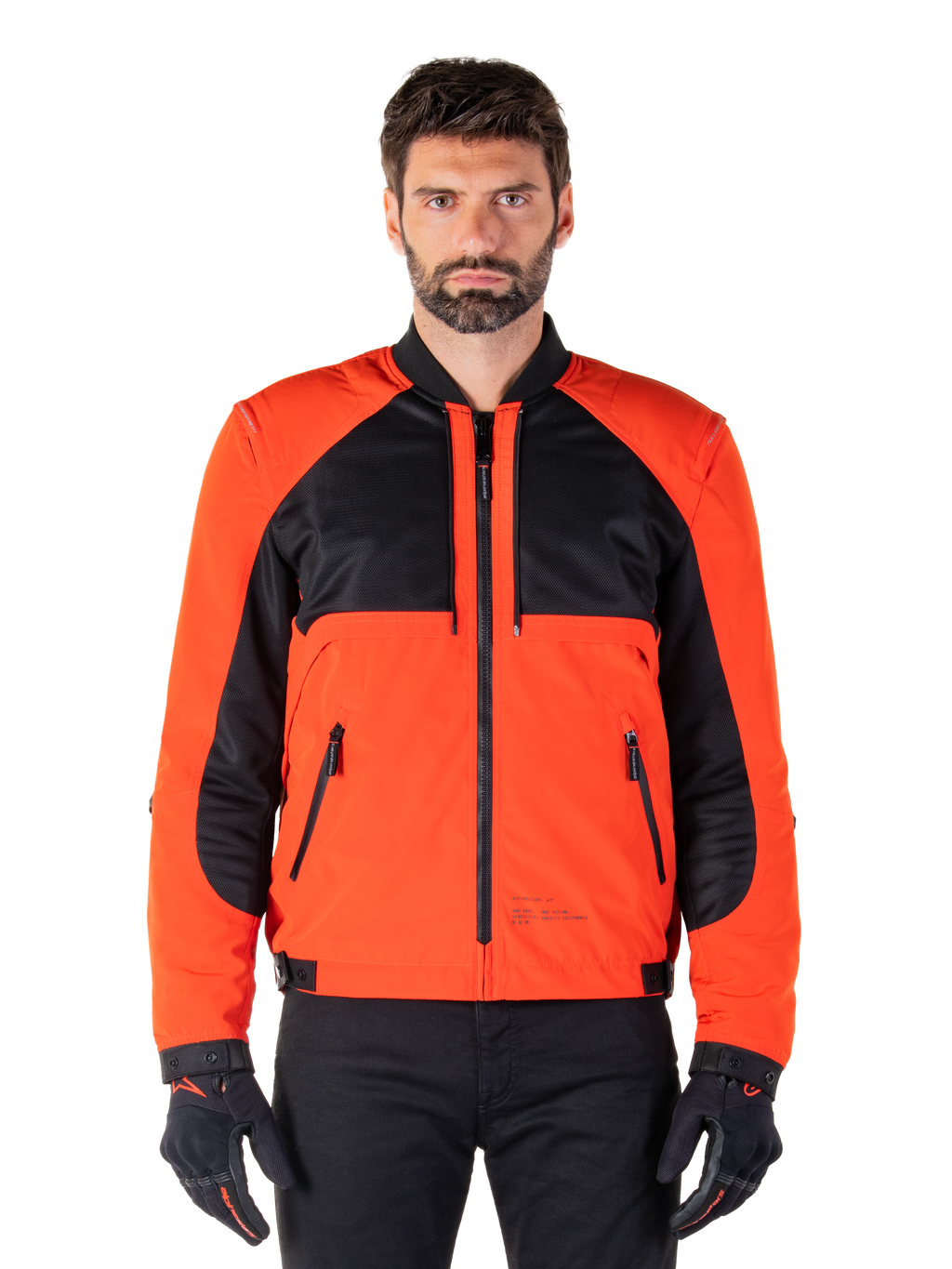 Alpinestars Mootant Waterproof Parka in Spicy Orange and Black, modular motorcycle jacket shown in a bomber-style configuration on a male model, featuring black mesh upper chest panels, bright orange torso and sleeves, front zipper, and ribbed collar, paired with black gloves and trousers