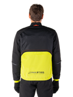 Parka imperméable Alpinestars Mootant, veste de moto, Lime Punch et noir, vue de dos présentant une partie supérieure en mesh noir pour la ventilation et une partie inférieure lime avec le logo MO.ST.EQ., portée avec un pantalon et des gants noirs