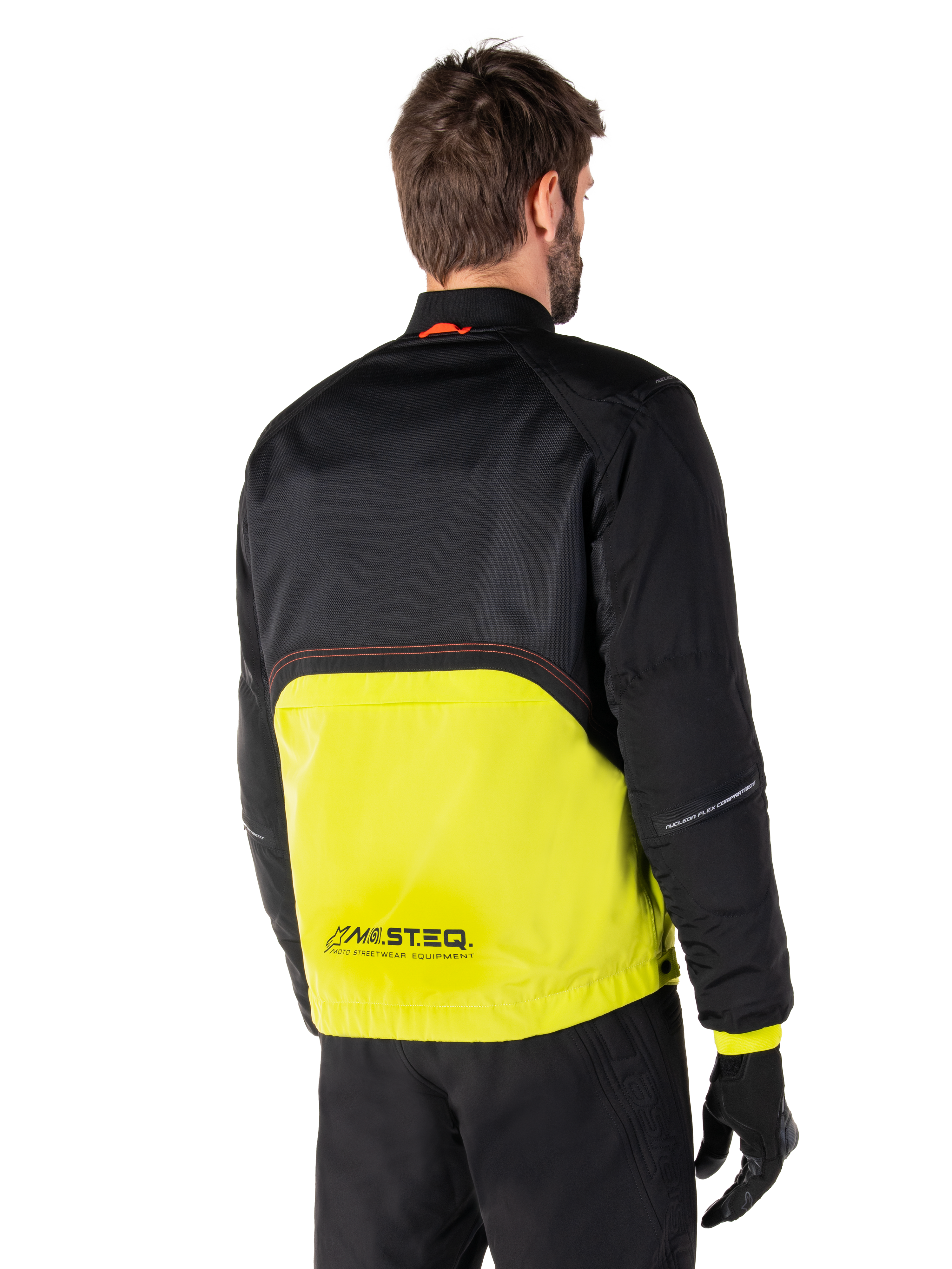 Parka imperméable Alpinestars Mootant, veste de moto, lime punch et noir, vue arrière montrant la partie supérieure en maille noire et la partie inférieure en vert lime éclatant, avec marquage MO.ST.EQ., portée avec un pantalon de moto et des gants noirs
