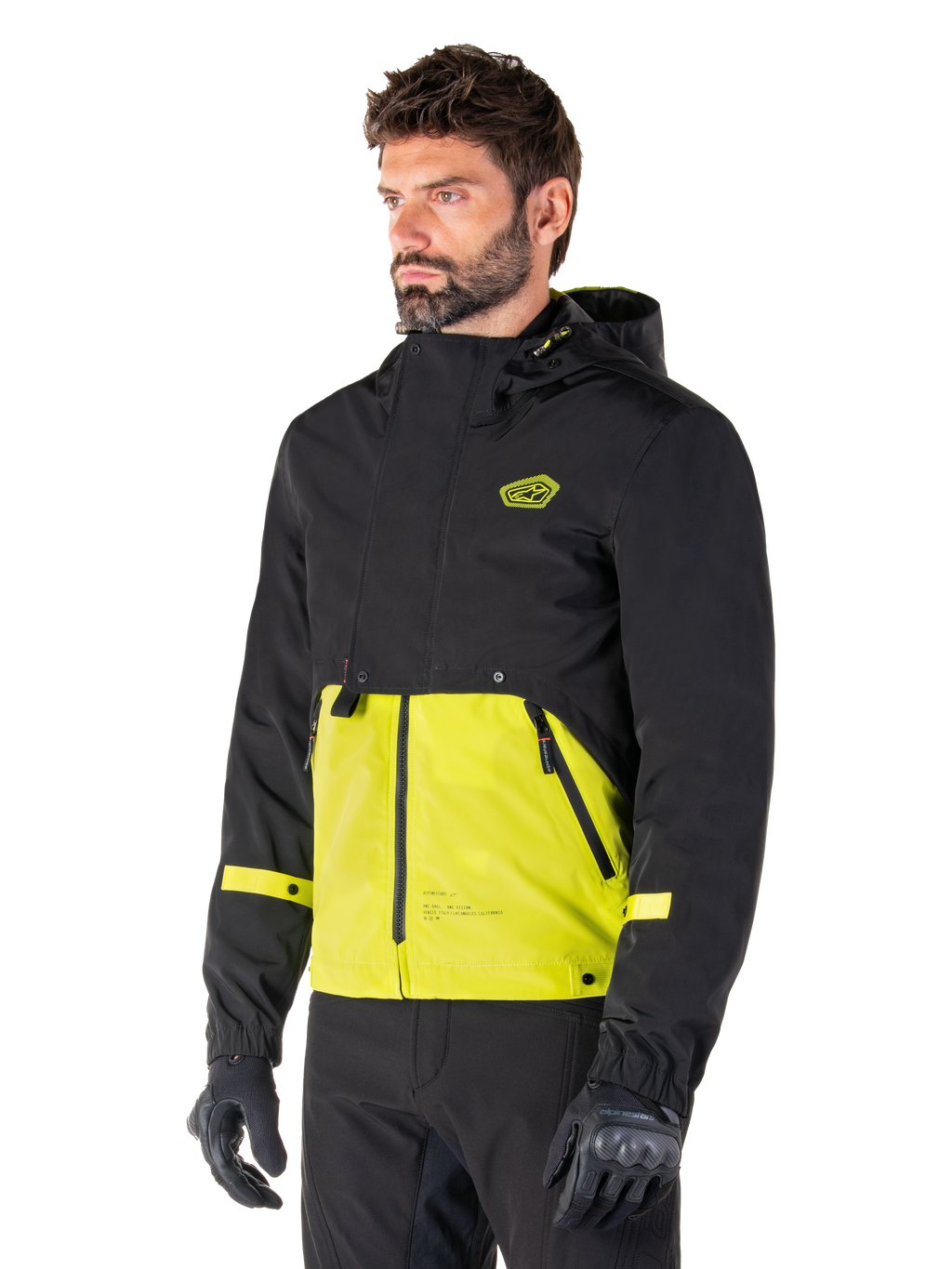 Parka imperméable Alpinestars Mootant en Lime Punch Black, veste de moto modulaire portée par un homme avec des gants et un pantalon de moto noirs, dotée d'une section supérieure et de manches noires avec un empiècement inférieur vert citron éclatant, design à capuche et esthétique utilitaire d'inspiration militaire.