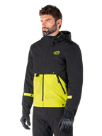 Parka imperméable Alpinestars Mootant en Lime Punch Black, veste de moto modulaire portée par un homme avec des gants et un pantalon de moto noirs, dotée d'une section supérieure et de manches noires avec un empiècement inférieur vert citron éclatant, design à capuche et esthétique utilitaire d'inspiration militaire.