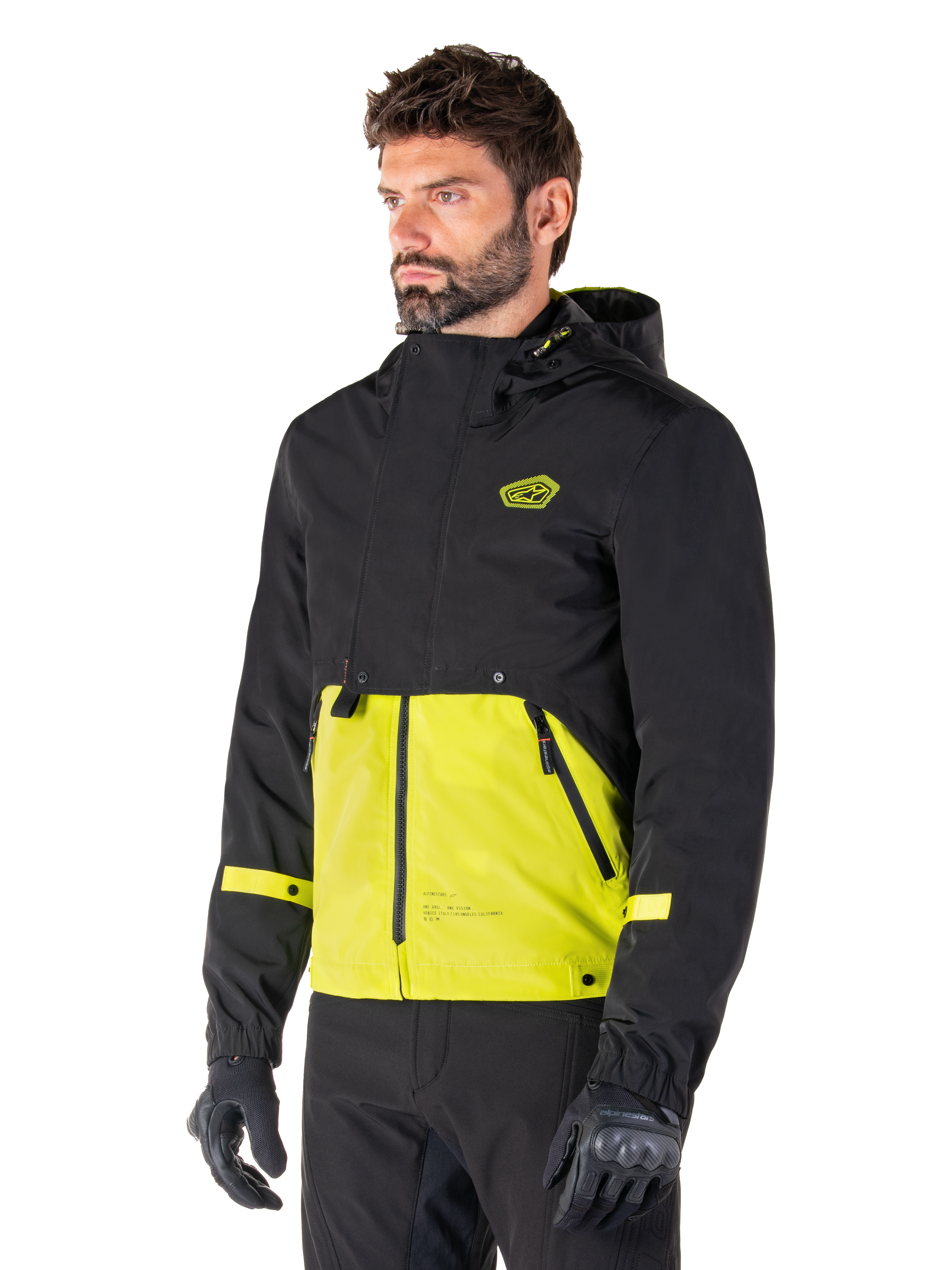 Parka imperméable Alpinestars Mootant en Lime Punch Black, veste de moto modulaire portée par un homme avec des gants et un pantalon de moto noirs, dotée d'une section supérieure et de manches noires avec un empiècement inférieur vert citron éclatant, design à capuche et esthétique utilitaire d'inspiration militaire.
