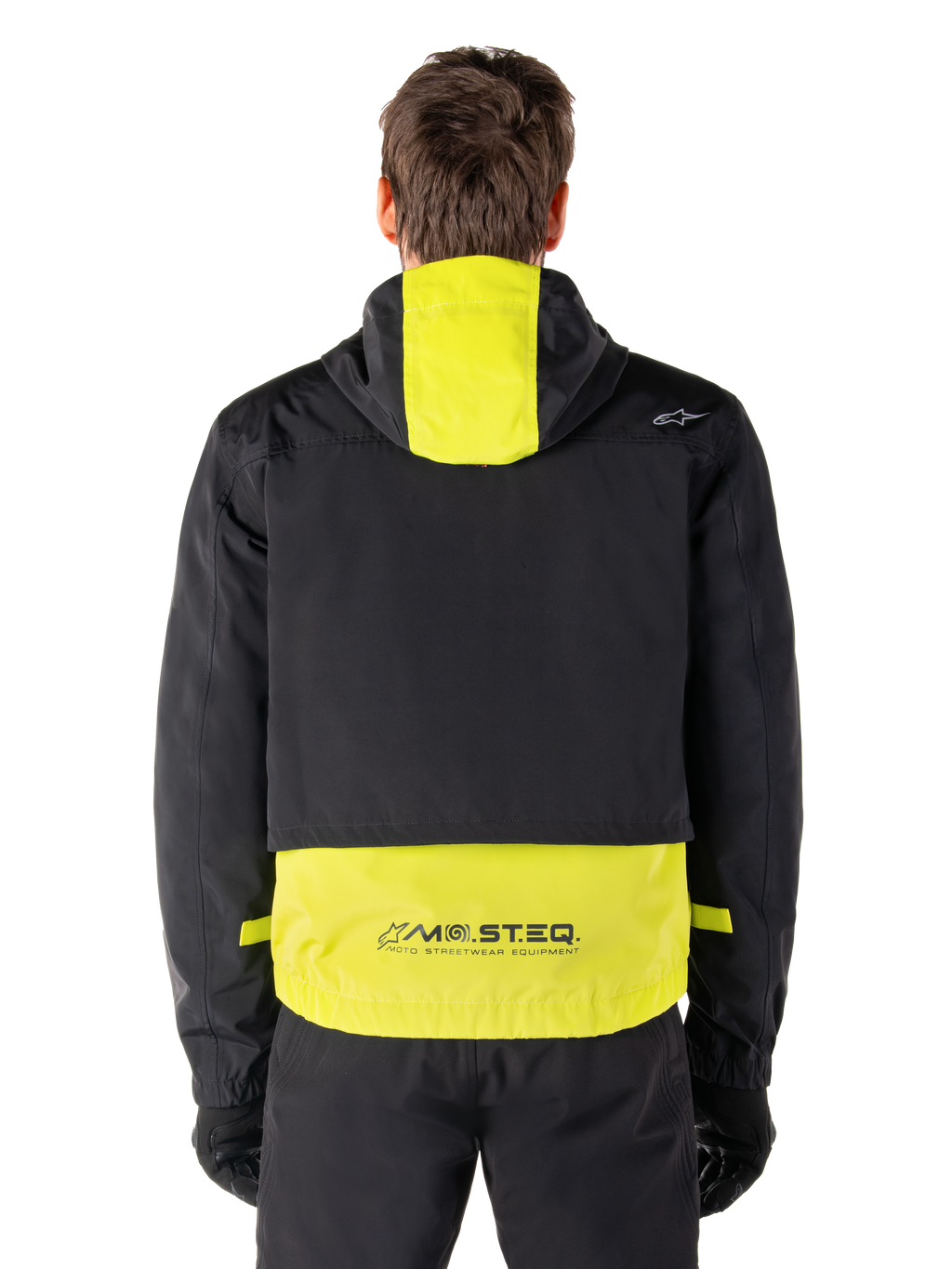 Alpinestars Mootant Waterproof Parka, veste de moto, Lime Punch et noir, vue arrière montrant la capuche et le logo réfléchissant MO.ST.EQ. dans le bas du dos, portée avec un pantalon de moto et des gants noirs.