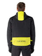 Alpinestars Mootant Waterproof Parka, veste de moto, Lime Punch et noir, vue arrière montrant la capuche et le logo réfléchissant MO.ST.EQ. dans le bas du dos, portée avec un pantalon de moto et des gants noirs.