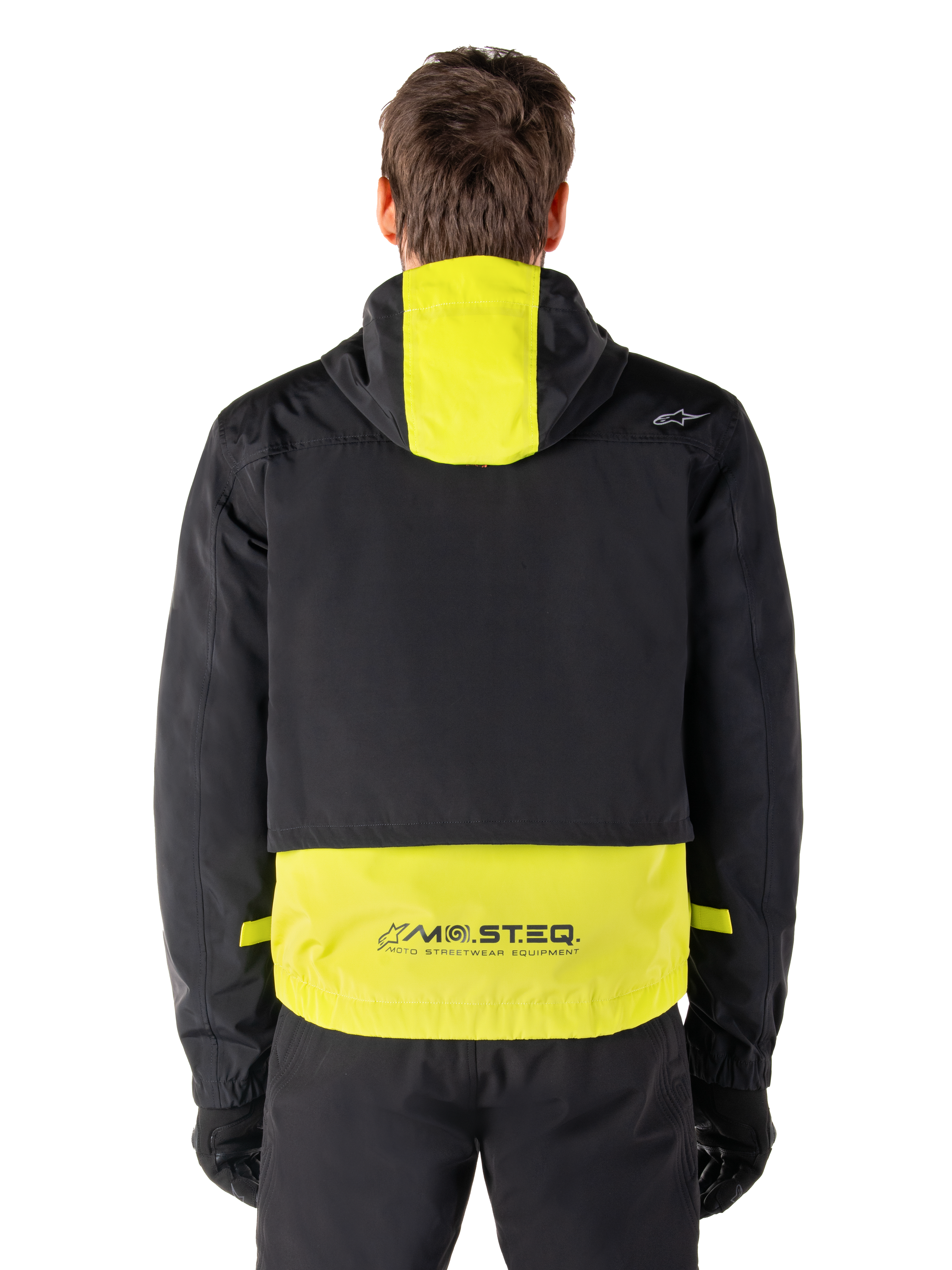 Alpinestars Mootant Waterproof Parka, veste de moto, Lime Punch et noir, vue arrière montrant la capuche et le logo réfléchissant MO.ST.EQ. dans le bas du dos, portée avec un pantalon de moto et des gants noirs.