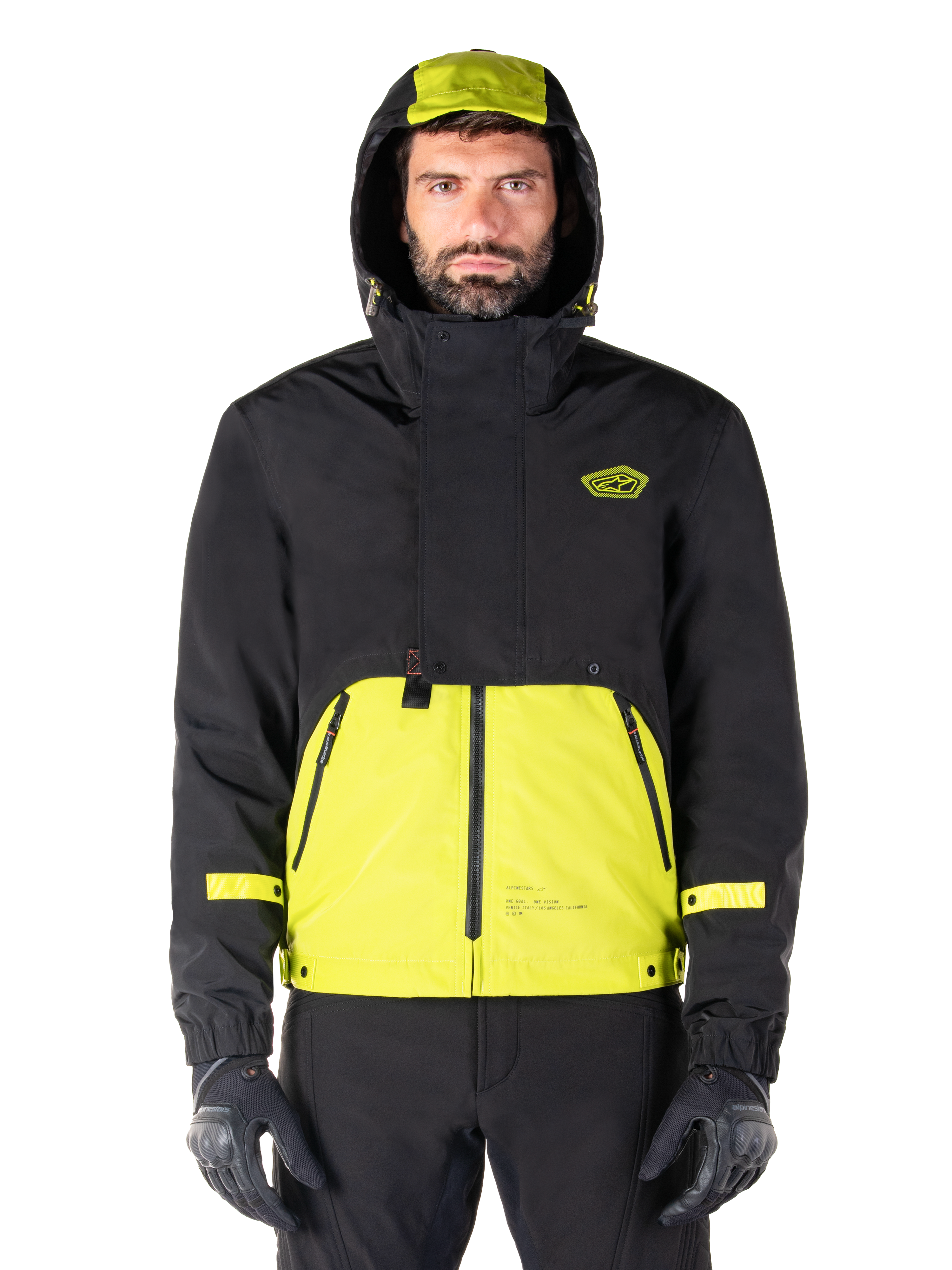 Parka imperméable Alpinestars Mootant, veste de moto Lime Punch Black, vue de face, conception modulaire 3-en-1 avec partie supérieure noire et section inférieure vert citron éclatant, dotée d'une capuche à cordon de serrage et d'un logo sur la poitrine, portée avec un pantalon noir et des gants de moto