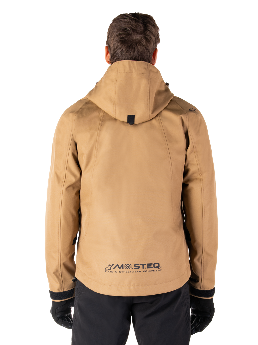 Alpinestars Morush Waterproof Parka, Utility Brown, rear view, featuring a hood and MO.ST.EQ. branding on the lower back, paired with black pants and gloves, modern streetwear-inspired motorcycle gear