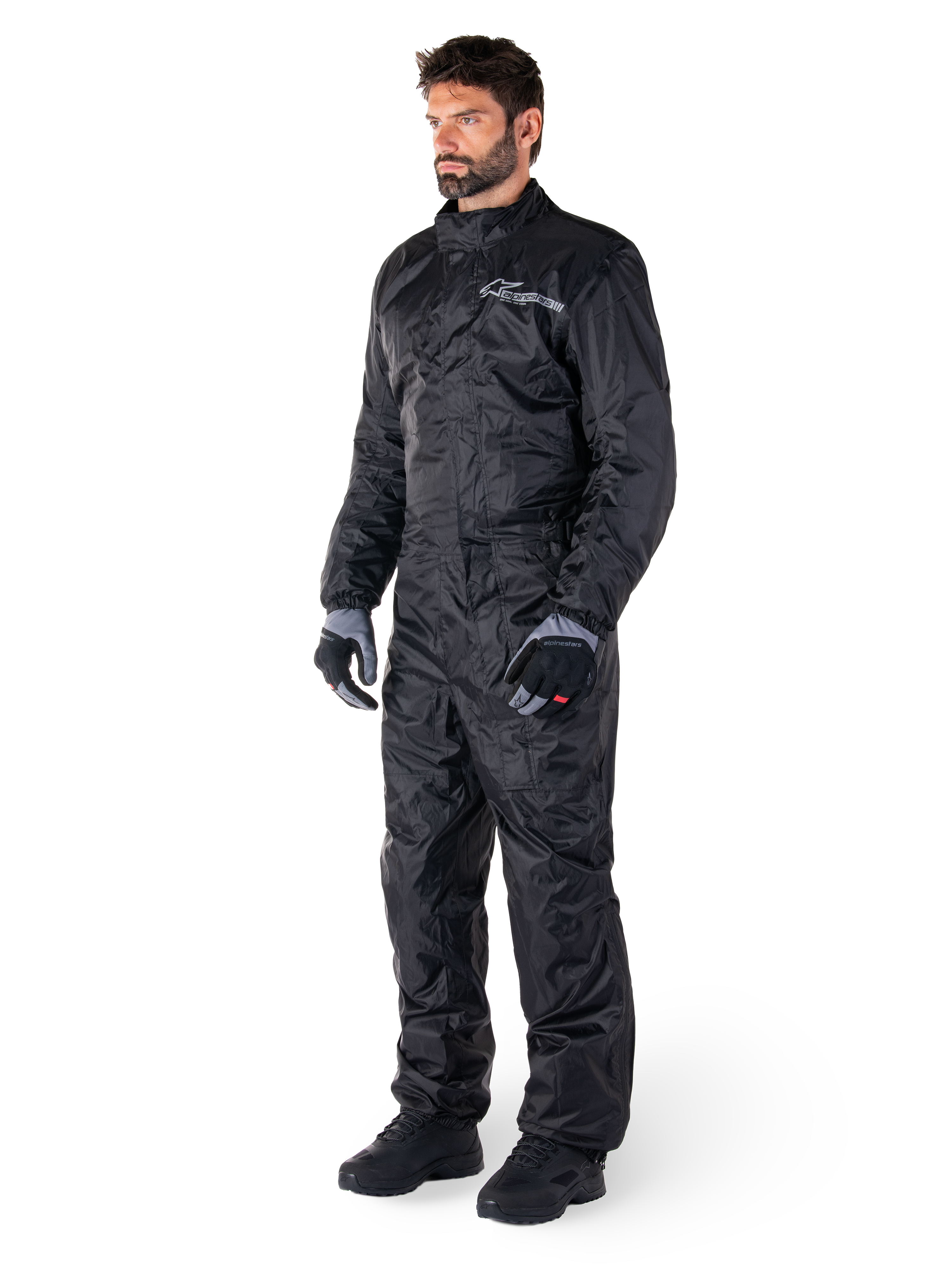 Alpinestars Hurricane Rain V2 Suit, Black, one-piece waterproof motorcycle rain suit, worn with gloves and boots, featuring reflective Alpinestars branding on the chest, lightweight design for wet weather protection