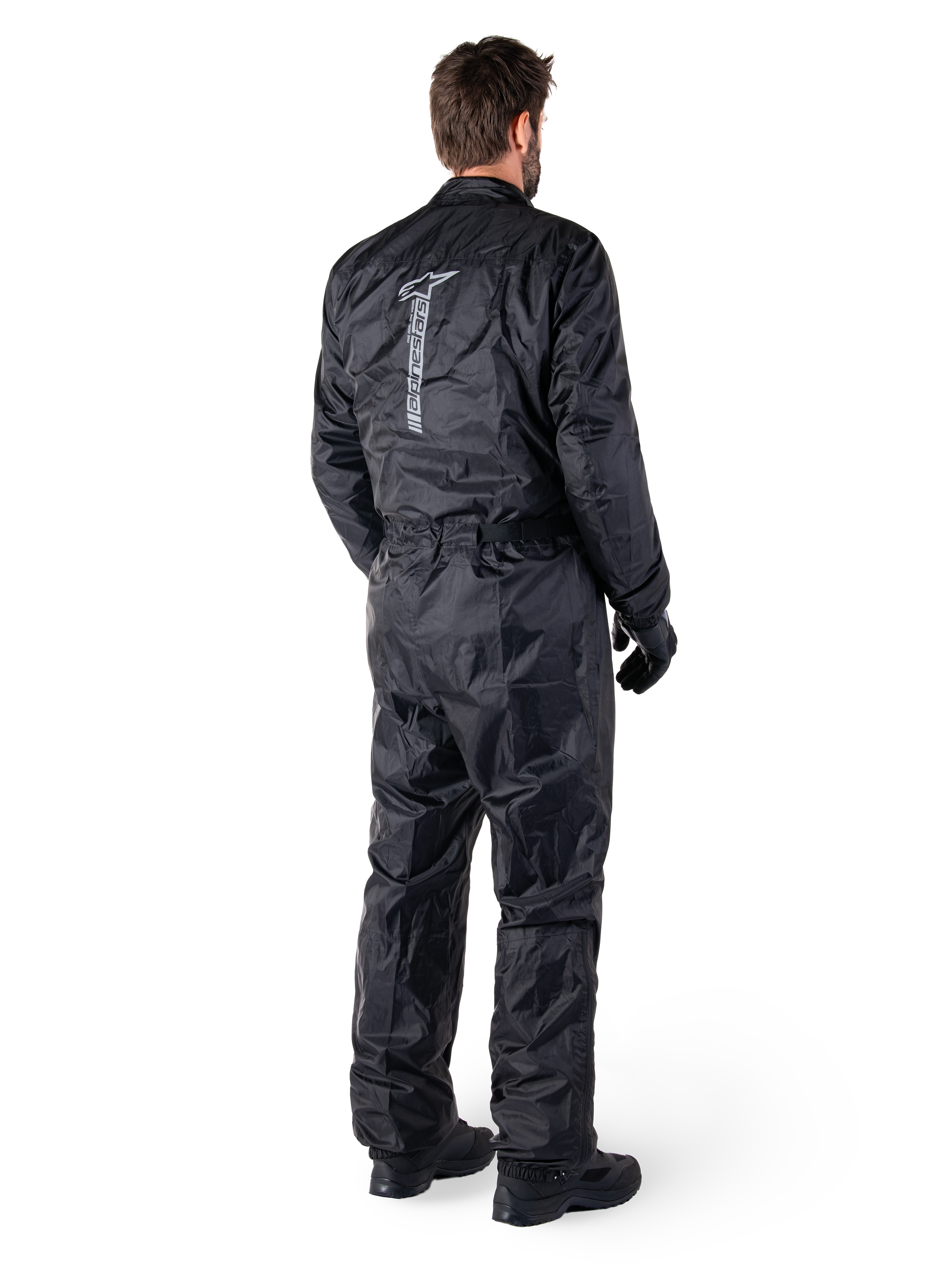 Alpinestars Hurricane Rain V2 Suit, Black one-piece waterproof motorcycle rain suit, back view with large vertical reflective logo, lightweight wind-resistant fabric, worn with black gloves and boots