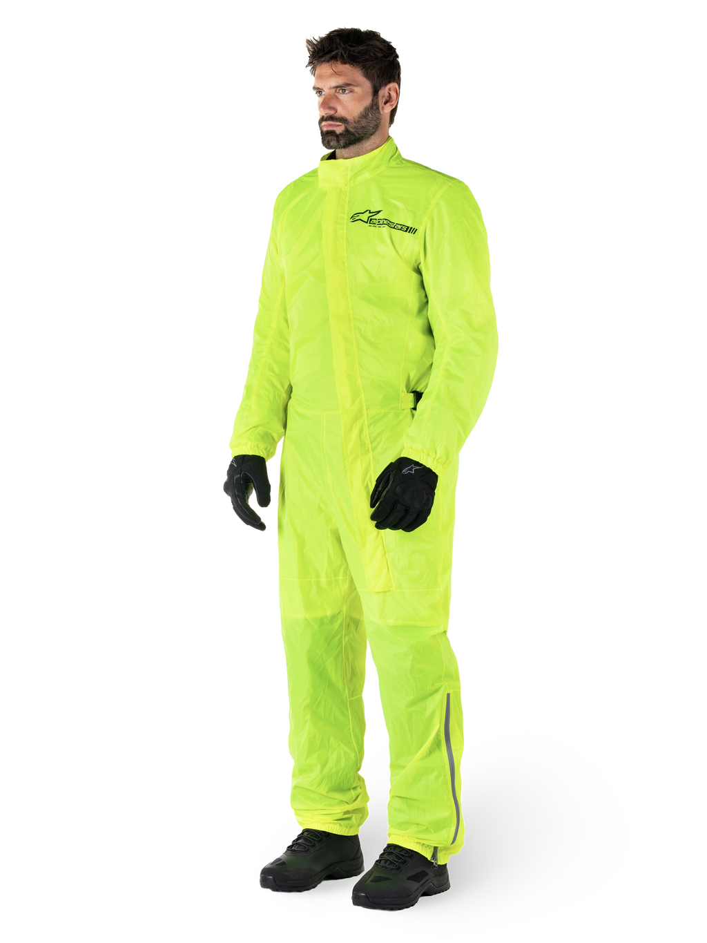 Combinaison Alpinestars Hurricane Rain V2, combinaison de moto imperméable une pièce, jaune fluo, portée avec des gants et des bottes noirs, avec un logo Alpinestars noir sur la poitrine et des détails réfléchissants sur les jambes