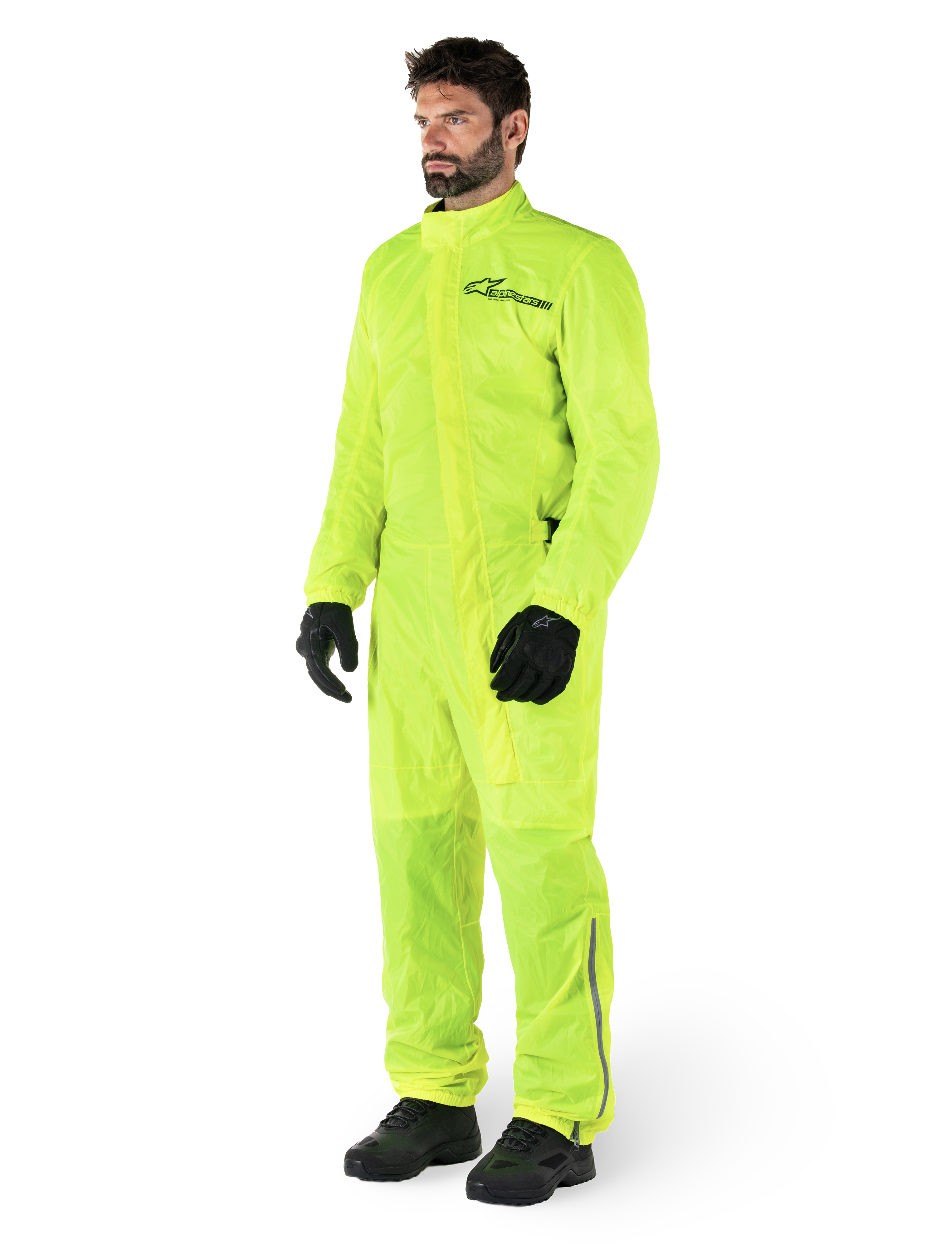 Combinaison Alpinestars Hurricane Rain V2, combinaison de moto imperméable une pièce, jaune fluo, portée avec des gants et des bottes noirs, avec un logo Alpinestars noir sur la poitrine et des détails réfléchissants sur les jambes