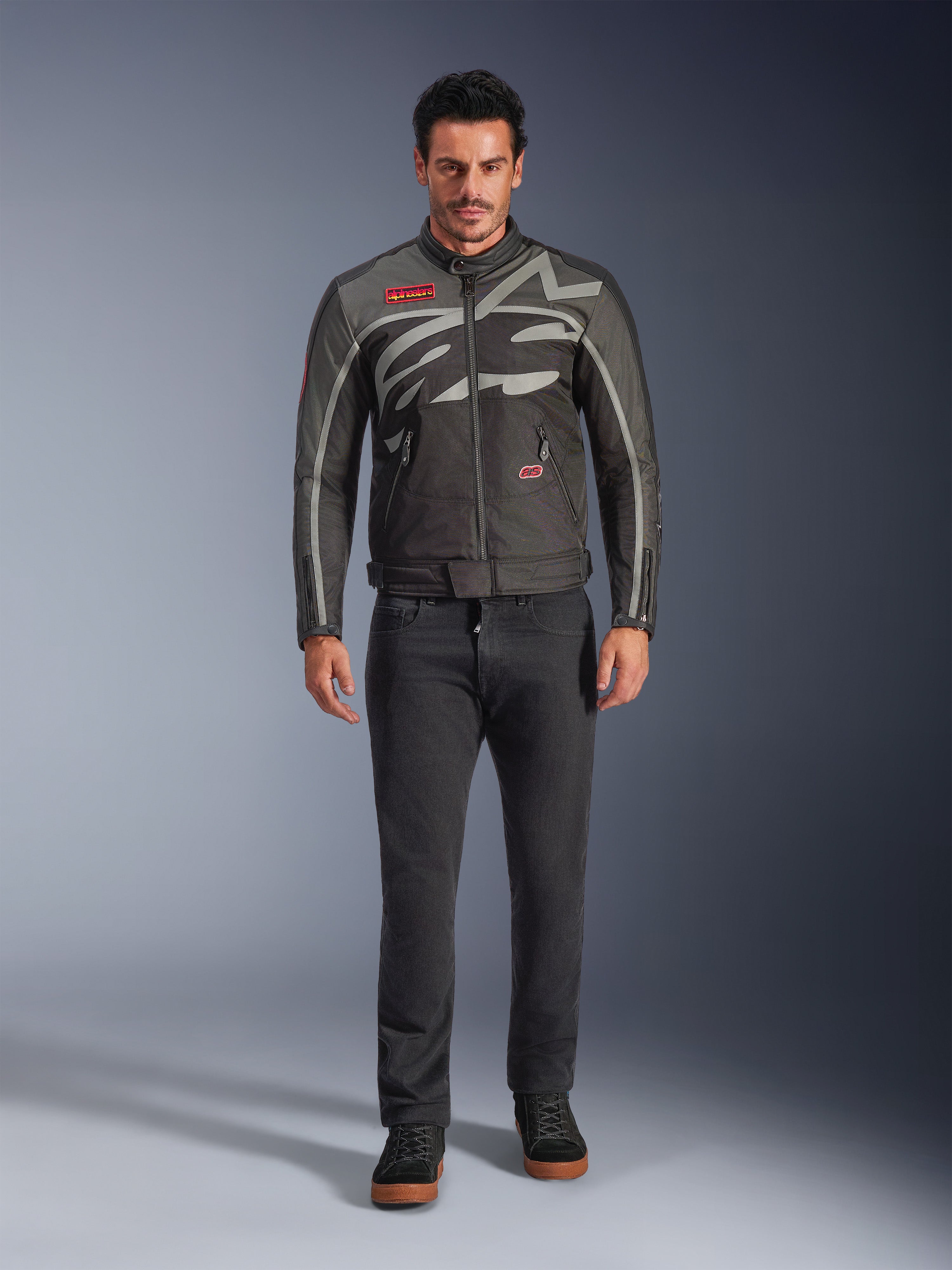 Veste Alpinestars Axton, veste de moto, Noir Anthracite Rouge Tangerine, portée par un mannequin avec un pantalon sombre, dotée d'un logo Alpinestars gris enveloppant, de patchs rouges de la marque et d'une coque en textile résistante à l'eau pour la conduite urbaine