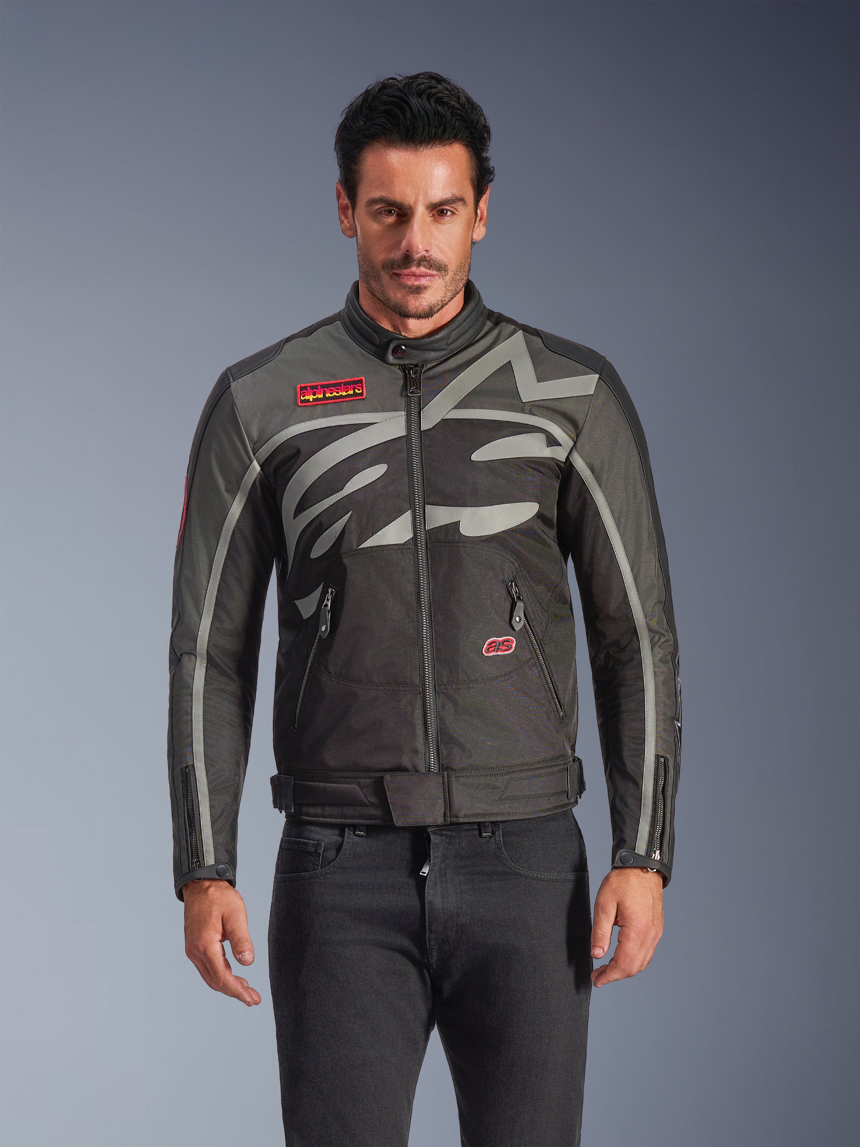 Veste Alpinestars Axton, veste de moto urbaine pour homme, noir et anthracite avec des touches de rouge, dotée d'un large motif graphique gris clair enveloppant, écussons avec logo rouge sur la poitrine et la poche, fermeture éclair frontale et poignets zippés, design de course d'inspiration vintage pour la conduite urbaine