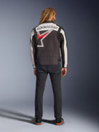Veste Alpinestars Axton, veste de moto, noir, blanc cassé et rouge vif, vue de dos sur un mannequin, avec un grand logo étoile Alpinestars dans le dos, empiècements de manches blanc cassé, portée avec un pantalon noir, design inspiré des vêtements d'équipe de course vintage