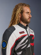 Homme aux cheveux longs et barbu portant la veste Alpinestars Axton, veste de moto, noir, blanc cassé et rouge vif, design d'inspiration racing vintage avec écussons de la marque et logo enveloppant, vue de profil rapprochée, style urbain contemporain