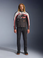 Veste Alpinestars Axton, veste de moto, noir, blanc cassé et rouge vif, portée par un mannequin avec un pantalon noir et des baskets, dotée d'un logo enveloppant audacieux et d'un design inspiré de la course vintage