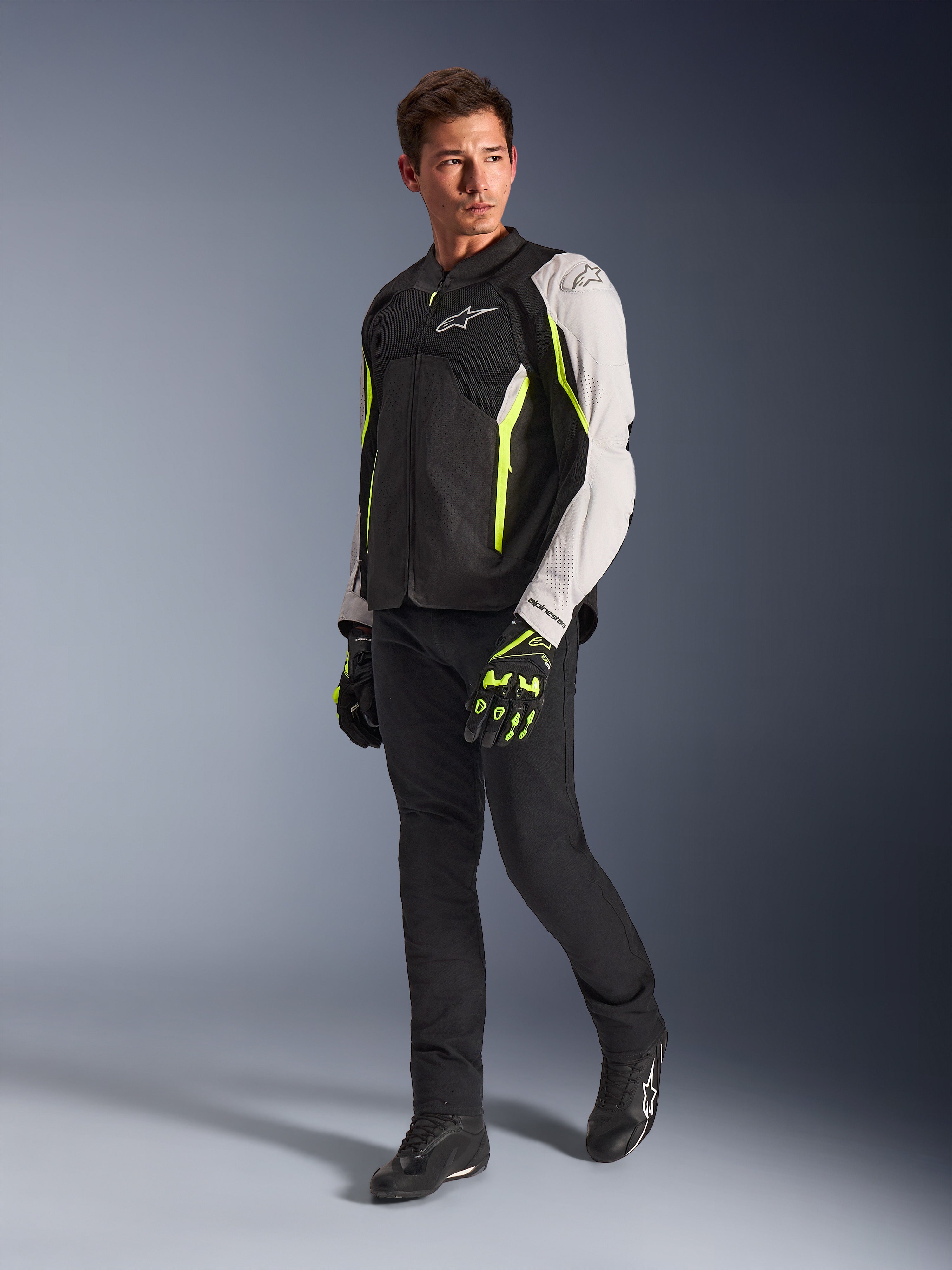 Veste Alpinestars AST V3 Air, veste de moto légère en textile, noir, argent et jaune fluo, portée par un mannequin avec un pantalon noir et des gants assortis, dotée de panneaux en mesh et de perforations au laser pour la conduite sportive par temps chaud.