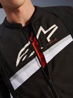 Veste Alpinestars T-GP Plus R V4, gros plan sur le torse et le col, textile noir avec logo étoile blanc et marquage T-GP PLUS, bande horizontale blanche et grise, fermeture éclair ouverte révélant une languette intérieure rouge avec l'inscription Tech-Air Ready