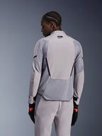 Veste Alpinestars Aeroshell Airflow en Gris Moyen Anthracite, vue de dos montrant les panneaux en maille respirante et les perforations au laser, construction en softshell technique extensible avec un panneau arrière allongé, portée avec un pantalon gris assorti et des gants noirs pour un look sportif.