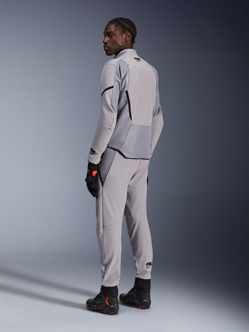 Veste Alpinestars Aeroshell Airflow en Mid Gray Anthracite, portée avec un pantalon assorti et des gants de course noirs, vue de dos montrant les panneaux perforés au laser et la coupe sport athlétique, équipement de moto professionnel