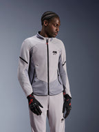 Veste Alpinestars Aeroshell Airflow, gris anthracite moyen, portée par un mannequin avec un pantalon textile assorti et des gants noirs avec des accents rouges, dotée de zones perforées au laser et de panneaux en maille pour la ventilation, design à coupe sportive pour la conduite moto.