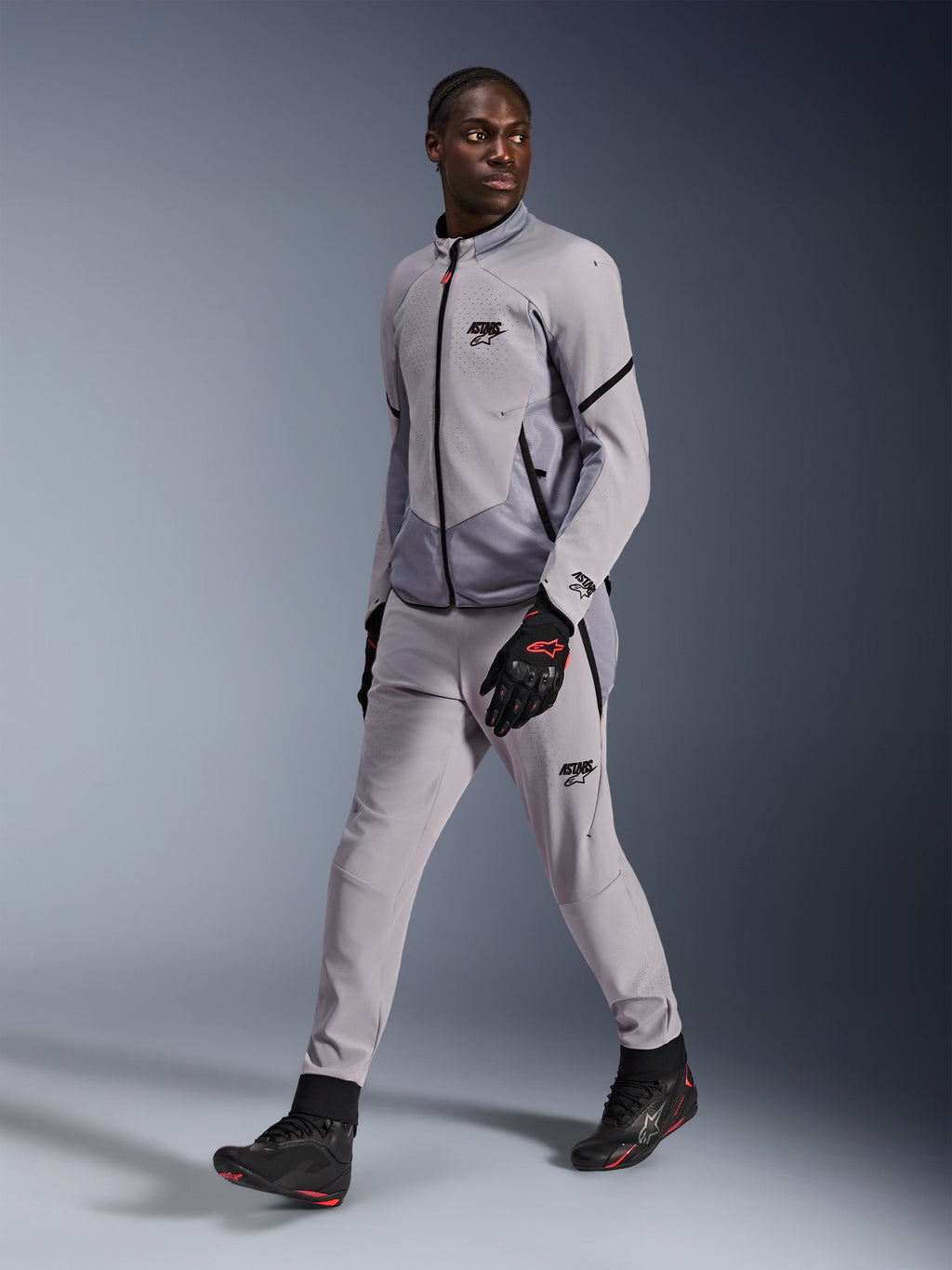 Veste Alpinestars Aeroshell Airflow en Gris Moyen Anthracite, portée par un mannequin homme avec un pantalon de moto gris assorti et des gants noirs, dotée d'une ventilation de poitrine perforée au laser et d'un design à coupe sportive.
