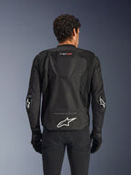 Alpinestars T-GP Air Jacket, noir, vue arrière d'un blouson de moto en textile, doté d'une bosse aérodynamique, de larges panneaux de ventilation en maille et d'un logo Alpinestars blanc dans le bas du dos, porté avec des gants et un pantalon de moto noirs