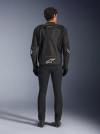 Alpinestars T-GP Air Jacket, noir, vue arrière d'un homme portant la veste de moto textile, présentant des panneaux de ventilation en maille, une bosse aérodynamique et des logos Alpinestars blancs sur le bas du dos et les coudes, portée avec un pantalon et des gants de moto noirs