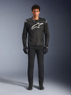 Veste Alpinestars T-GP Air, veste de moto en textile noir avec un grand logo Astars blanc sur la poitrine, portée par un mannequin avec un pantalon et des gants de moto noirs, dotée de panneaux perforés et d'une ventilation en mesh pour la conduite sportive