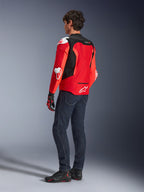 Veste Alpinestars T-GP Air, vue arrière d'un homme portant une veste textile rouge vif et rouge fluo avec des panneaux en maille noire et des sliders de protection blancs, associée à un jean bleu foncé et des chaussures de moto noires, équipement de moto sportive