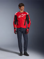 Veste Alpinestars T-GP Air, rouge vif, rouge fluo et noir, modèle masculin portant une tenue de moto complète avec jean bleu foncé et gants assortis, veste textile sportive avec panneaux en maille perforée et logo Astars blanc, photo de studio.