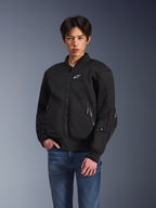 Veste Alpinestars Flight Air, veste de moto urbaine noire, portée par un homme avec un jean bleu, style bomber avec panneaux en maille, fermeture éclair frontale et logo blanc sur la poitrine, conçue pour la conduite urbaine par temps chaud