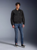 Veste Alpinestars Flight Air, noire, veste de moto de style bomber d'inspiration urbaine avec panneaux en maille 3D et logo blanc sur la poitrine, portée par un mannequin avec un jean bleu et des baskets noires, tenue de moto contemporaine