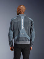Alpinestars Flight Air Jacket in Storm Gray, rear view on a model, urban motorcycle jacket featuring extended 3D mesh panels, vertical Alpinestars branding on the back, and a bomber-style ribbed hem and collar.