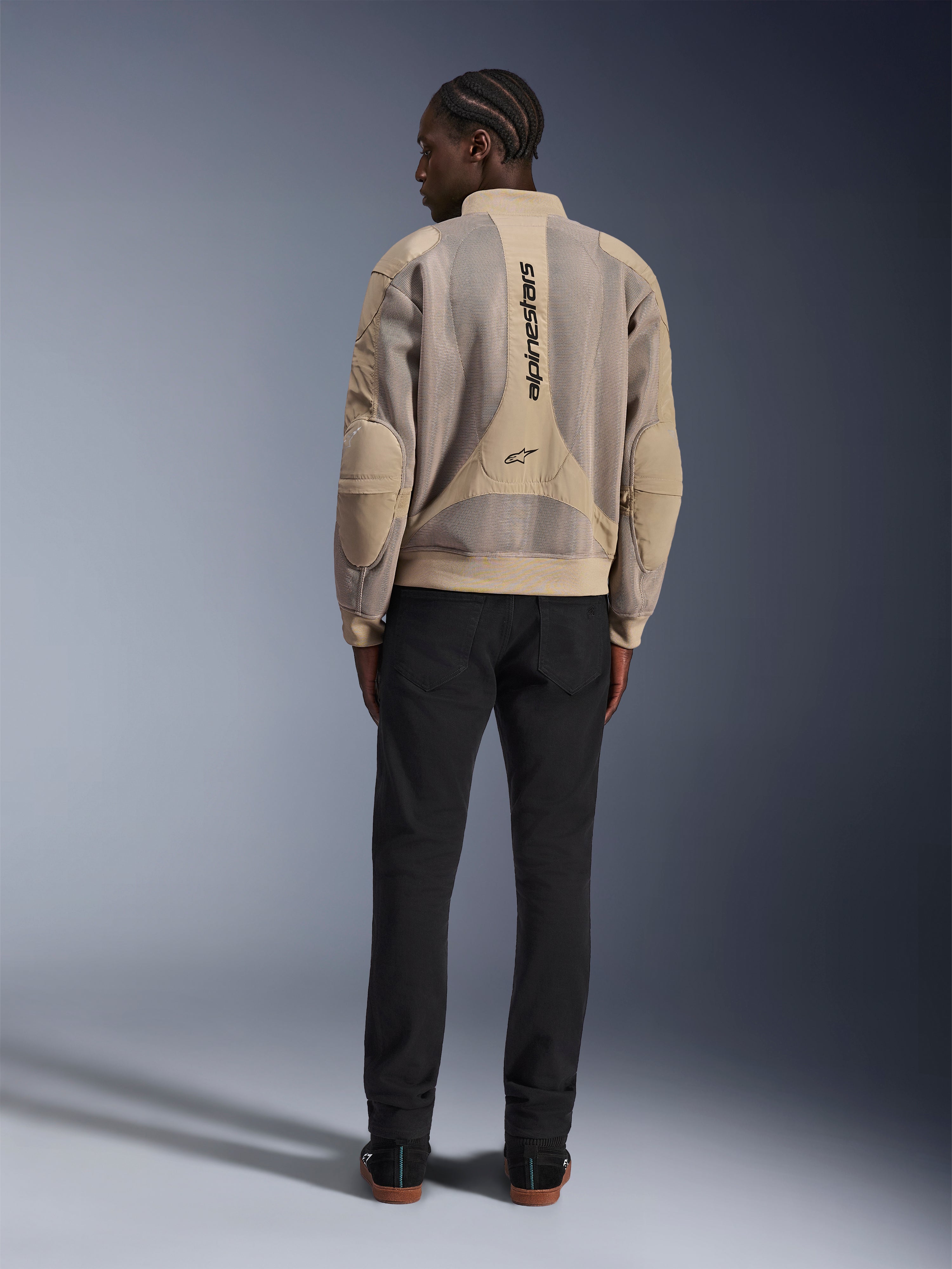 Veste Alpinestars Flight Air, veste de moto urbaine beige, vue arrière montrant les panneaux en maille 3D respirante et le logo vertical, portée avec un pantalon noir pour un look urbain moderne
