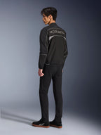 Veste Alpinestars Unite, veste de moto urbaine, noir et gris foncé, vue de dos montrant un grand logo Alpinestars à contours, lisérés et empiècements réfléchissants, design softshell minimaliste, portée avec un pantalon noir et des chaussures décontractées