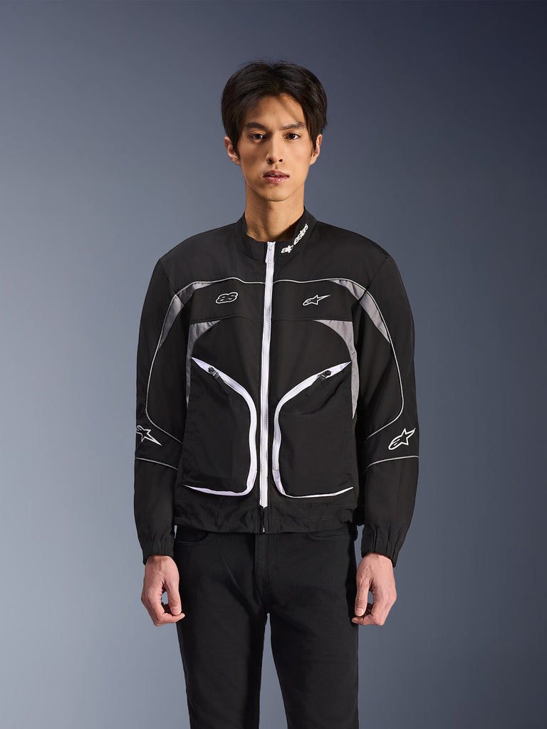 Alpinestars Unite Jacket, veste de moto urbaine, noire avec fermetures éclair et détails blancs, logos de marque, lignes courbes sur la poitrine, style moderne et sportif