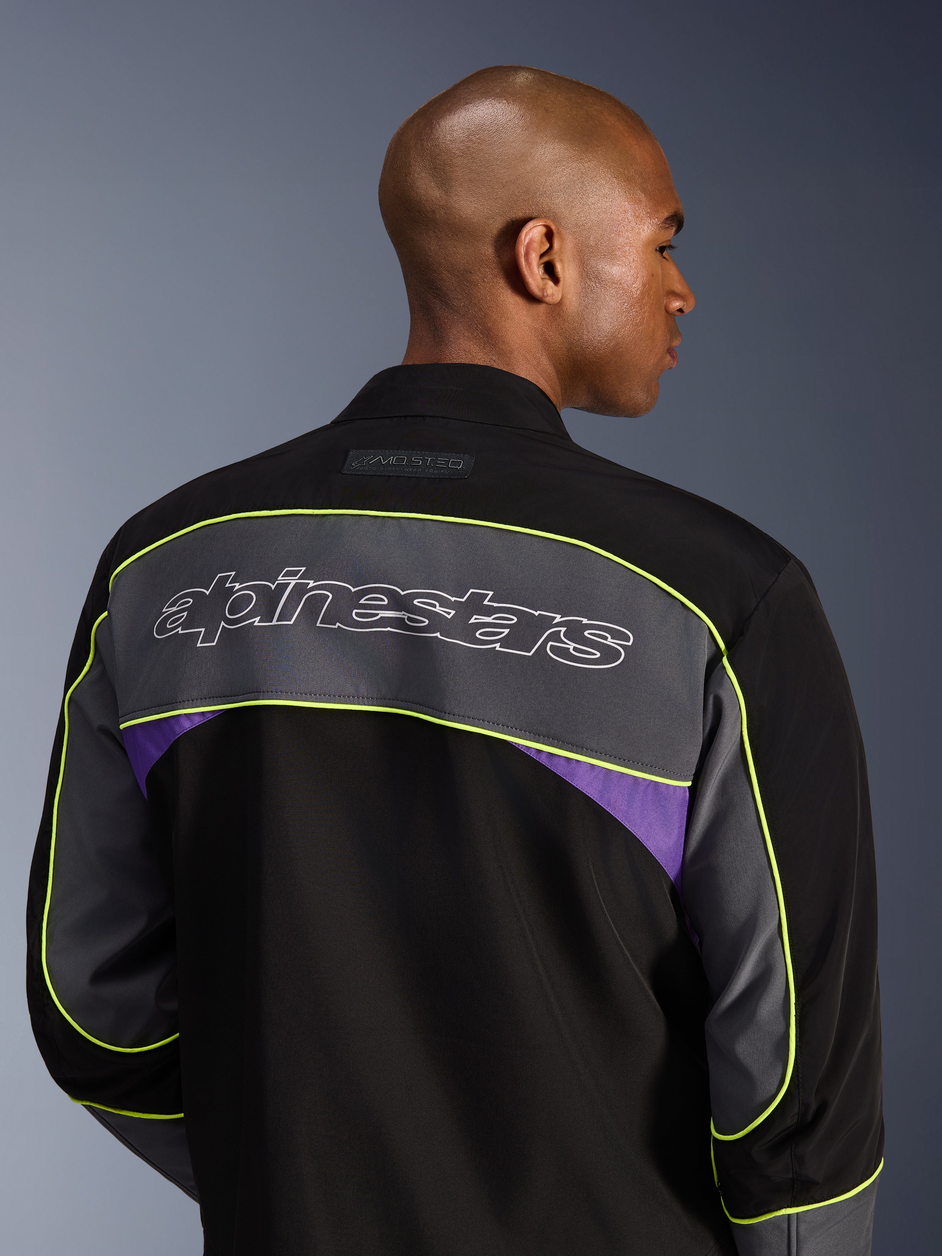 Alpinestars Unite Jacket, Urban Motorcycle Jacket, Black Asphalt Violet, back view showing a large grey shoulder panel with Alpinestars logo, neon yellow piping, and violet accents on a 3-layer softshell construction