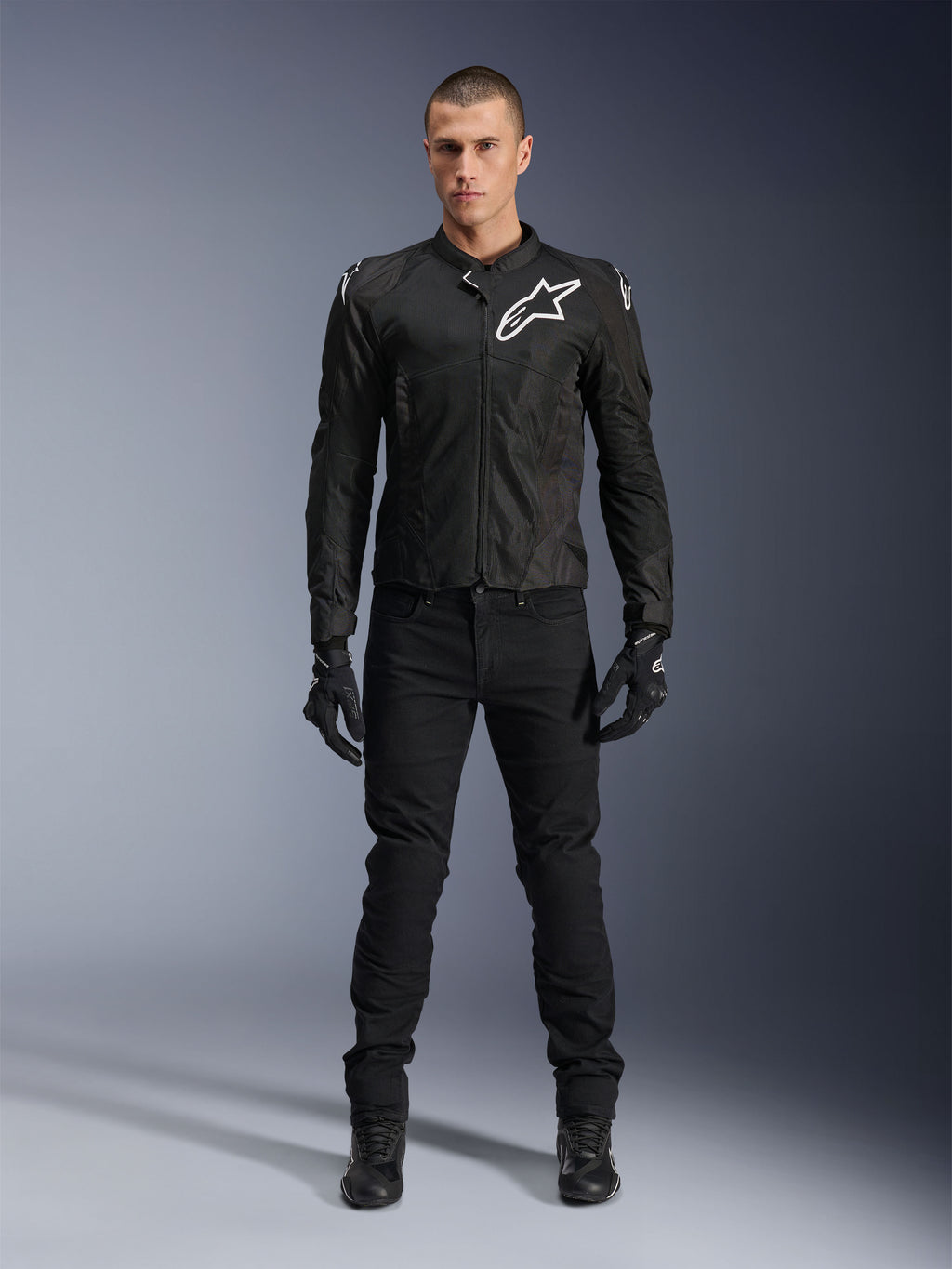 Veste Alpinestars Viper Air V4, veste de moto en textile noir, logo blanc sur la poitrine et les épaules, portée avec un pantalon de moto et des gants noirs, dotée de panneaux en maille technique pour la circulation de l'air, vue studio en pied