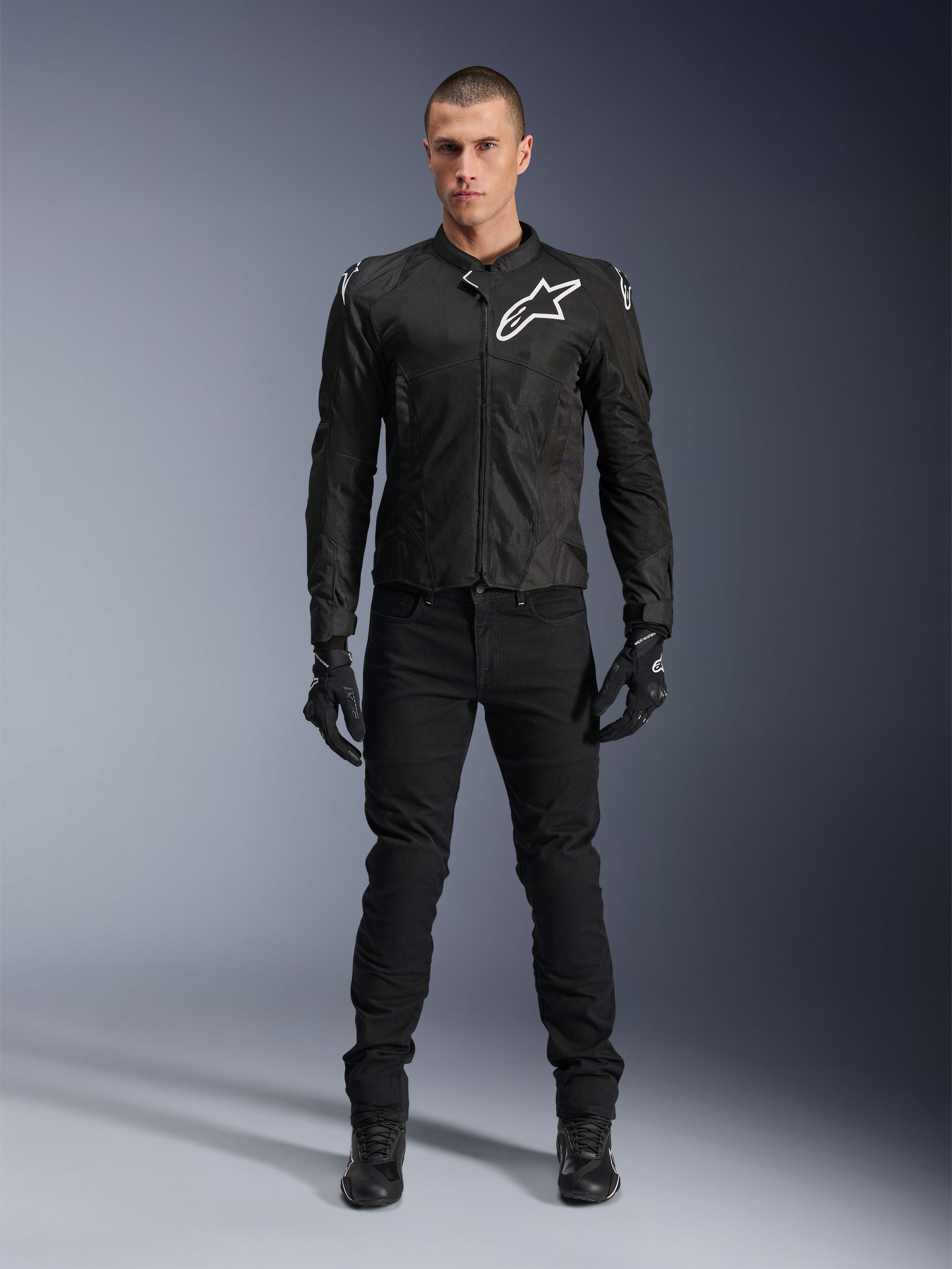 Veste Alpinestars Viper Air V4, veste de moto en textile noir, logo blanc sur la poitrine et les épaules, portée avec un pantalon de moto et des gants noirs, dotée de panneaux en maille technique pour la circulation de l'air, vue studio en pied