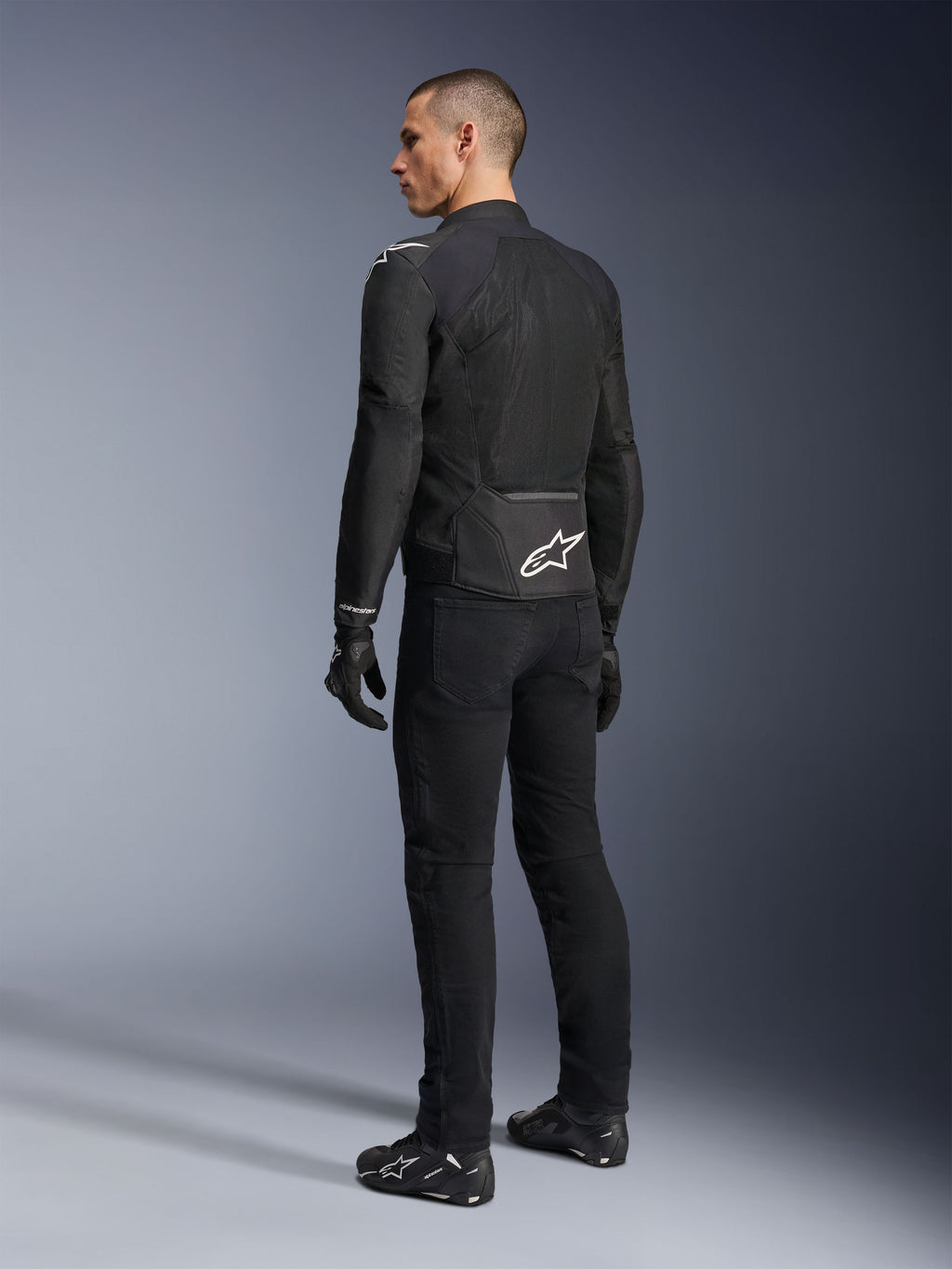 Veste Alpinestars Viper Air V4, veste de moto en textile noir, vue arrière sur un mannequin homme, dotée de larges panneaux en maille technique pour la circulation de l'air et d'un logo étoile blanche dans le bas du dos, portée avec un pantalon de moto et des gants noirs assortis.