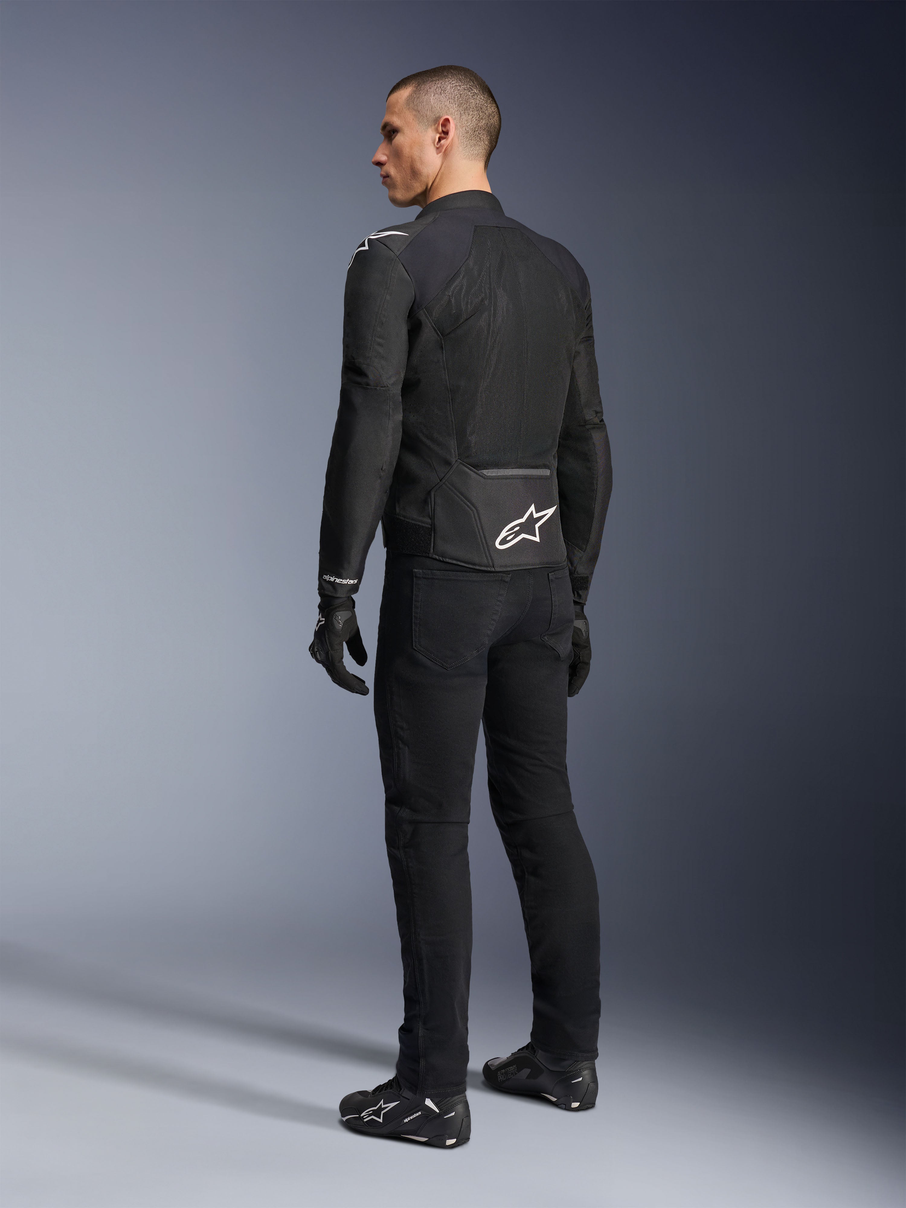Veste Alpinestars Viper Air V4, veste de moto en textile noir, vue arrière sur un mannequin homme, dotée de larges panneaux en maille technique pour la circulation de l'air et d'un logo étoile blanche dans le bas du dos, portée avec un pantalon de moto et des gants noirs assortis.