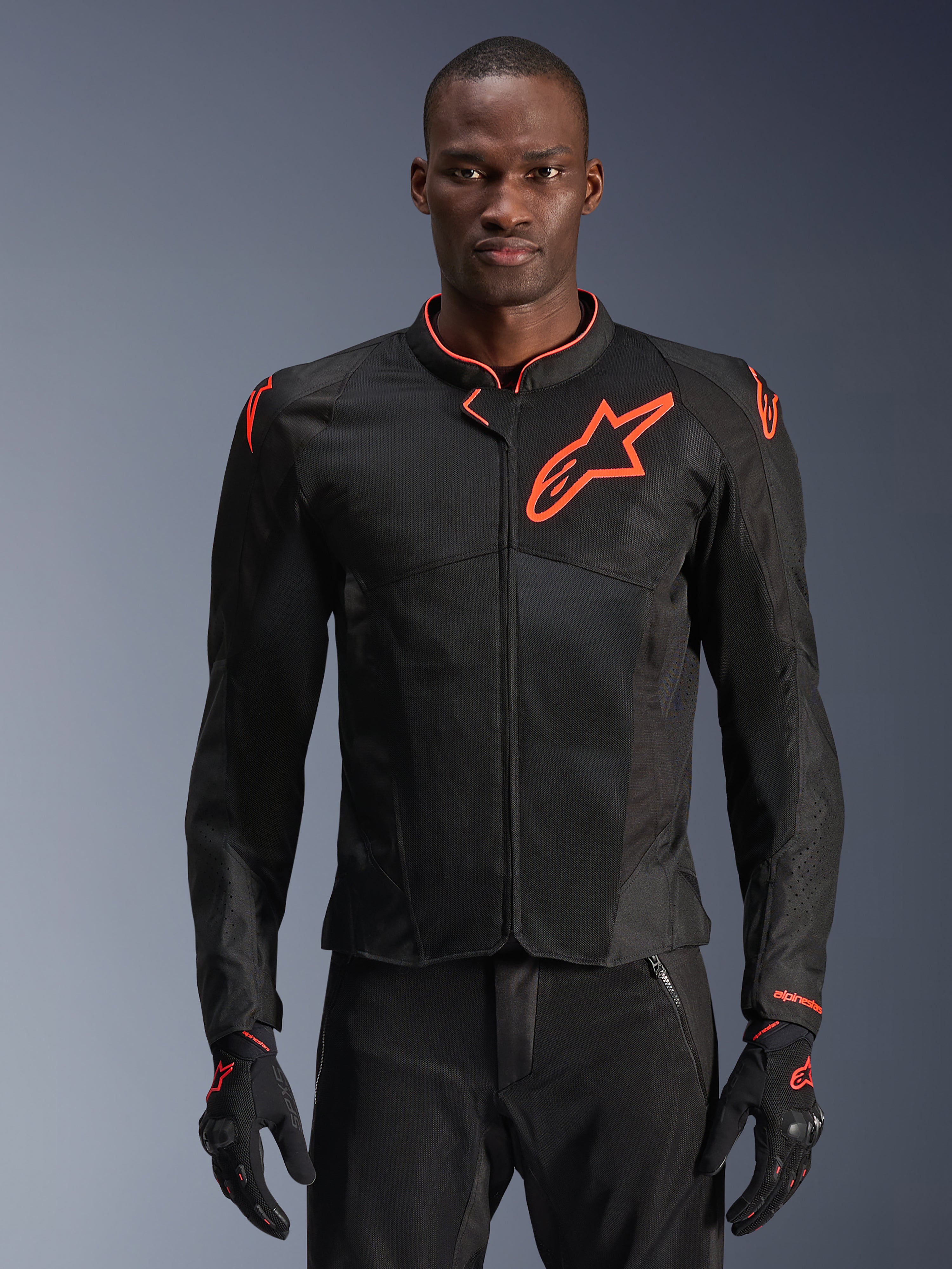 Veste Alpinestars Viper Air V4, veste de moto noire et rouge fluo, conception en mesh ventilé avec un logo étoile rouge proéminent, portée par un mannequin avec des gants assortis, design sportif haute performance