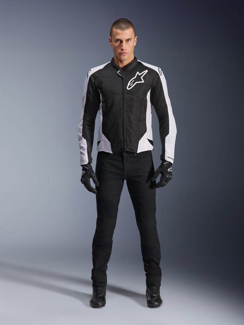 Veste Alpinestars Viper Air V4, veste de moto noire et blanche avec un grand logo blanc sur la poitrine, portée par un mannequin homme avec un pantalon noir et des gants, dotée de panneaux en maille pour la ventilation, vêtement de route sportif