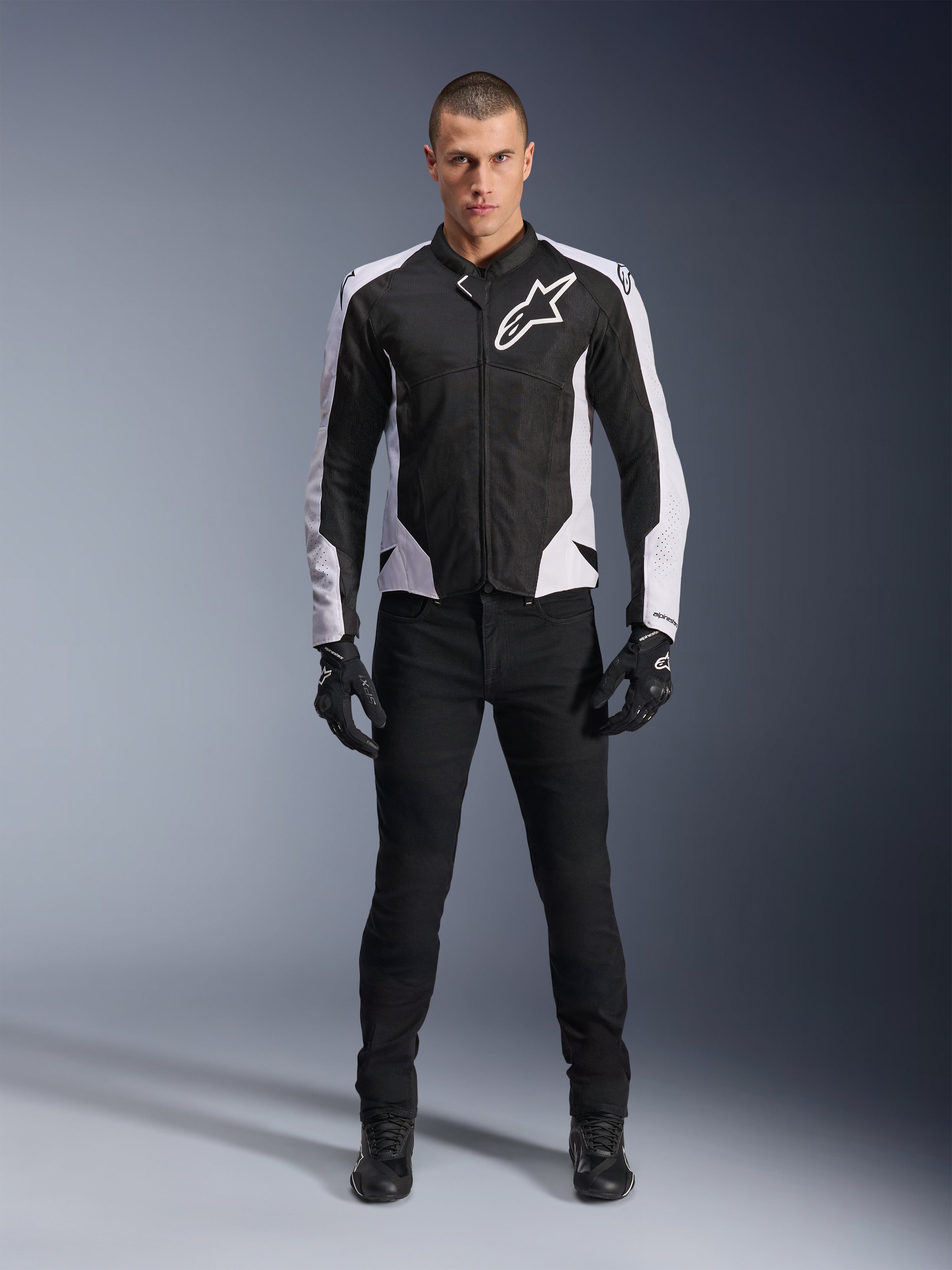 Veste Alpinestars Viper Air V4, veste de moto noire et blanche avec un grand logo blanc sur la poitrine, portée par un mannequin homme avec un pantalon noir et des gants, dotée de panneaux en maille pour la ventilation, vêtement de route sportif