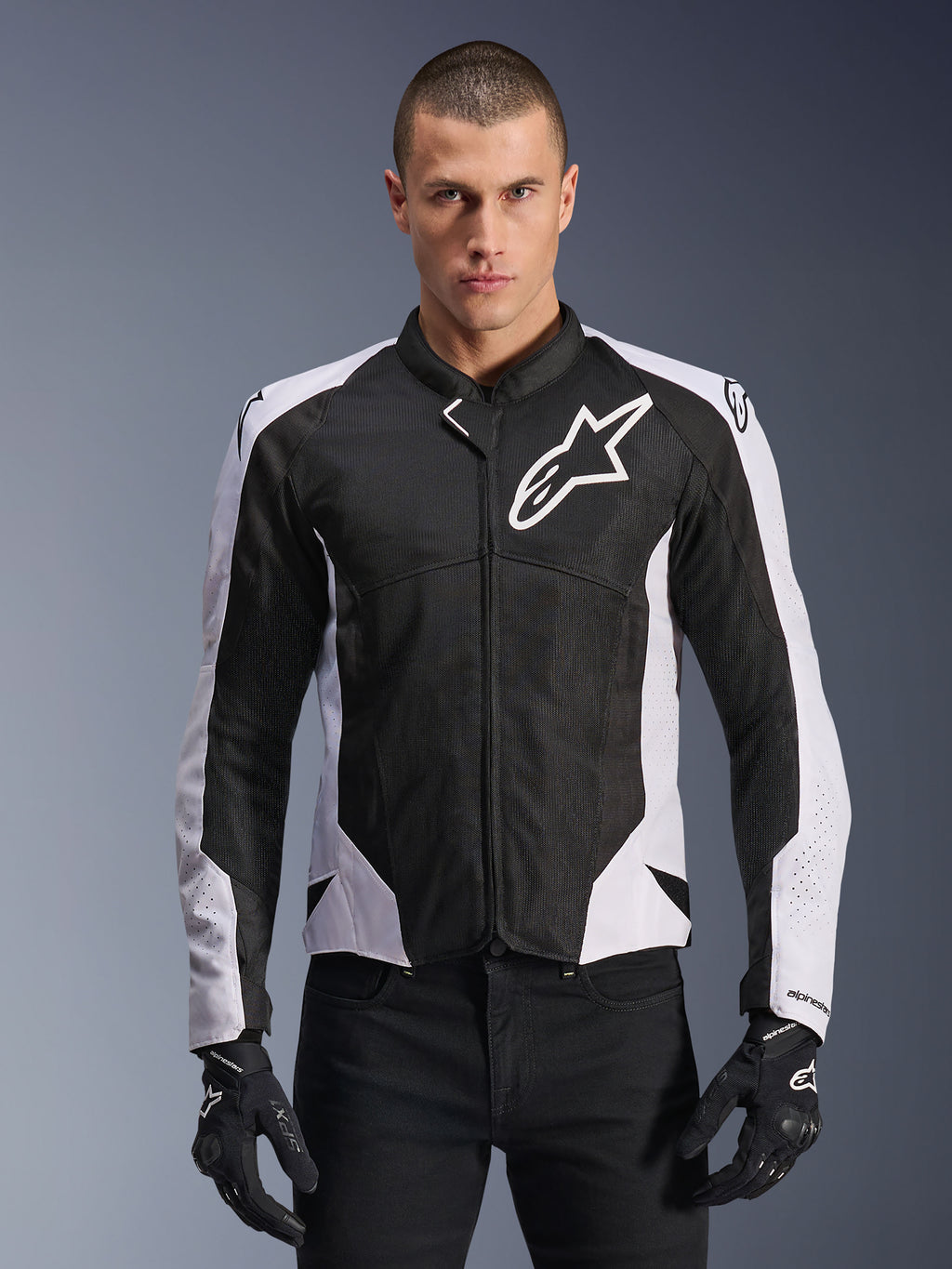 Veste Alpinestars Viper Air V4, veste de moto de course, noire et blanche, portée par un pilote, construction en maille technique et textile avec panneaux blancs aux épaules, logo étoile proéminent sur la poitrine, design sport haute performance, assortie à des gants de moto noirs