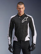 Veste Alpinestars Viper Air V4, veste de moto de course, noire et blanche, portée par un pilote, construction en maille technique et textile avec panneaux blancs aux épaules, logo étoile proéminent sur la poitrine, design sport haute performance, assortie à des gants de moto noirs