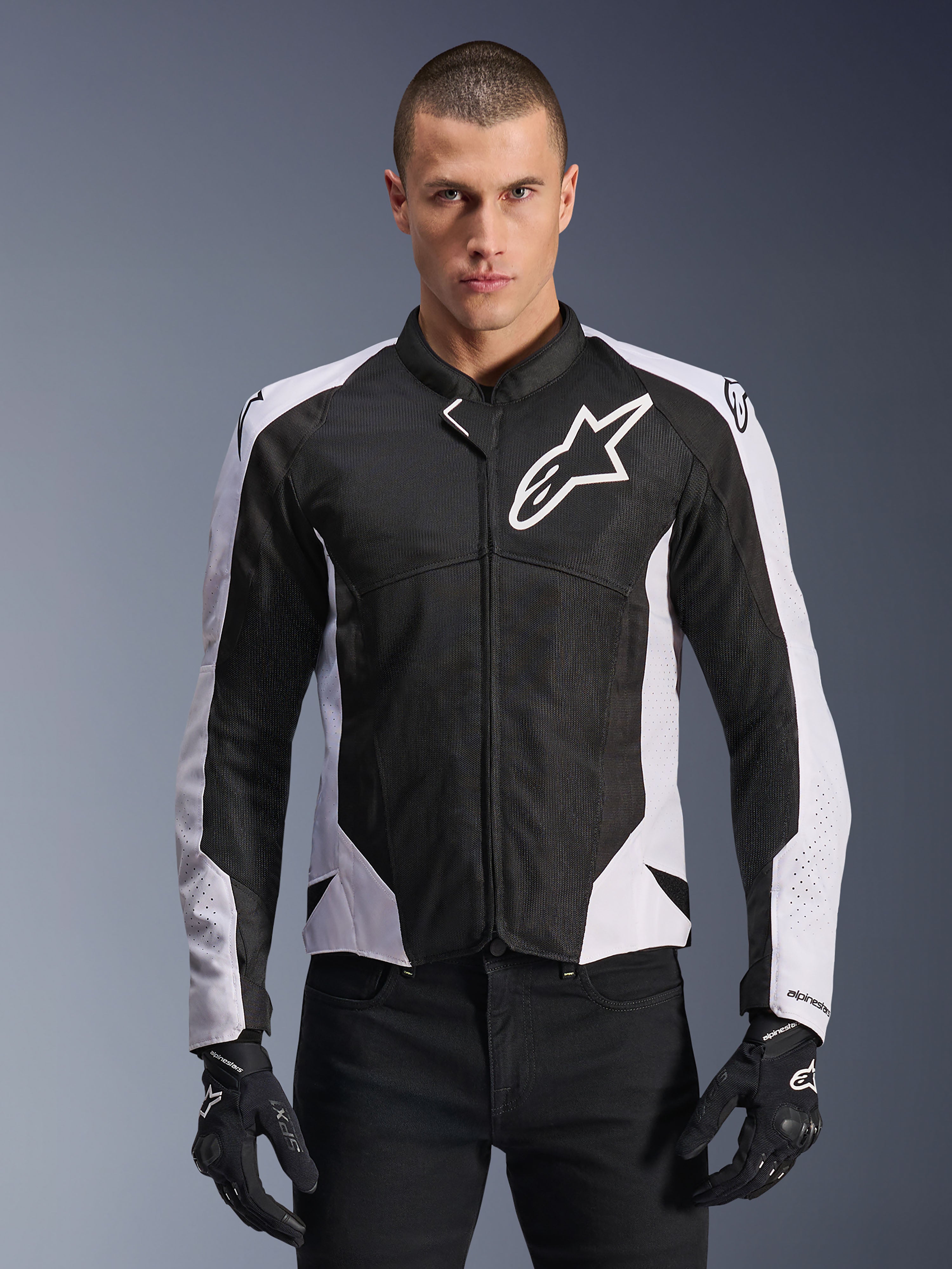 Veste Alpinestars Viper Air V4, veste de moto de course, noire et blanche, portée par un pilote, construction en maille technique et textile avec panneaux blancs aux épaules, logo étoile proéminent sur la poitrine, design sport haute performance, assortie à des gants de moto noirs