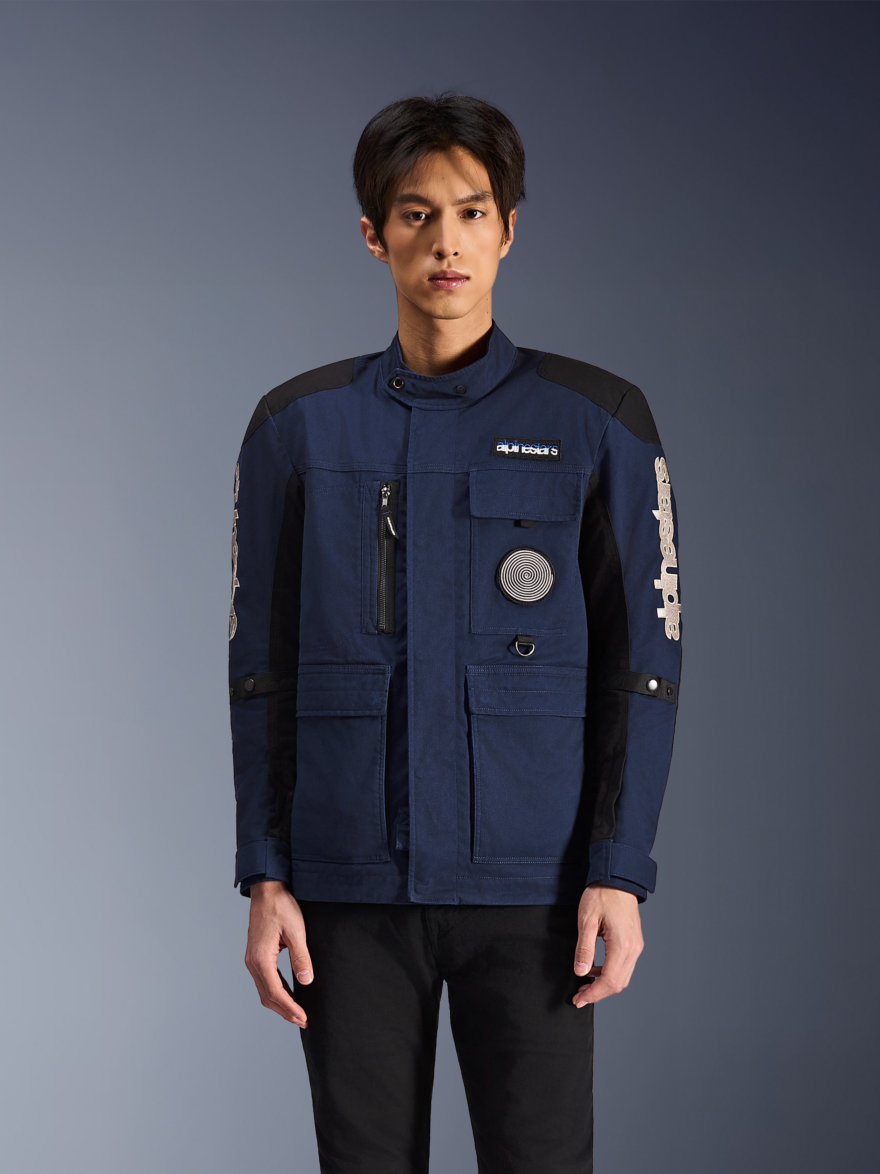 Alpinestars Dice Jacket, Urban Motorcycle Jacket, Dark Blue and Black, featuring a multi-pocket field jacket design with a spiral chest patch and white Alpinestars branding on the sleeves, modern workwear-inspired riding apparel