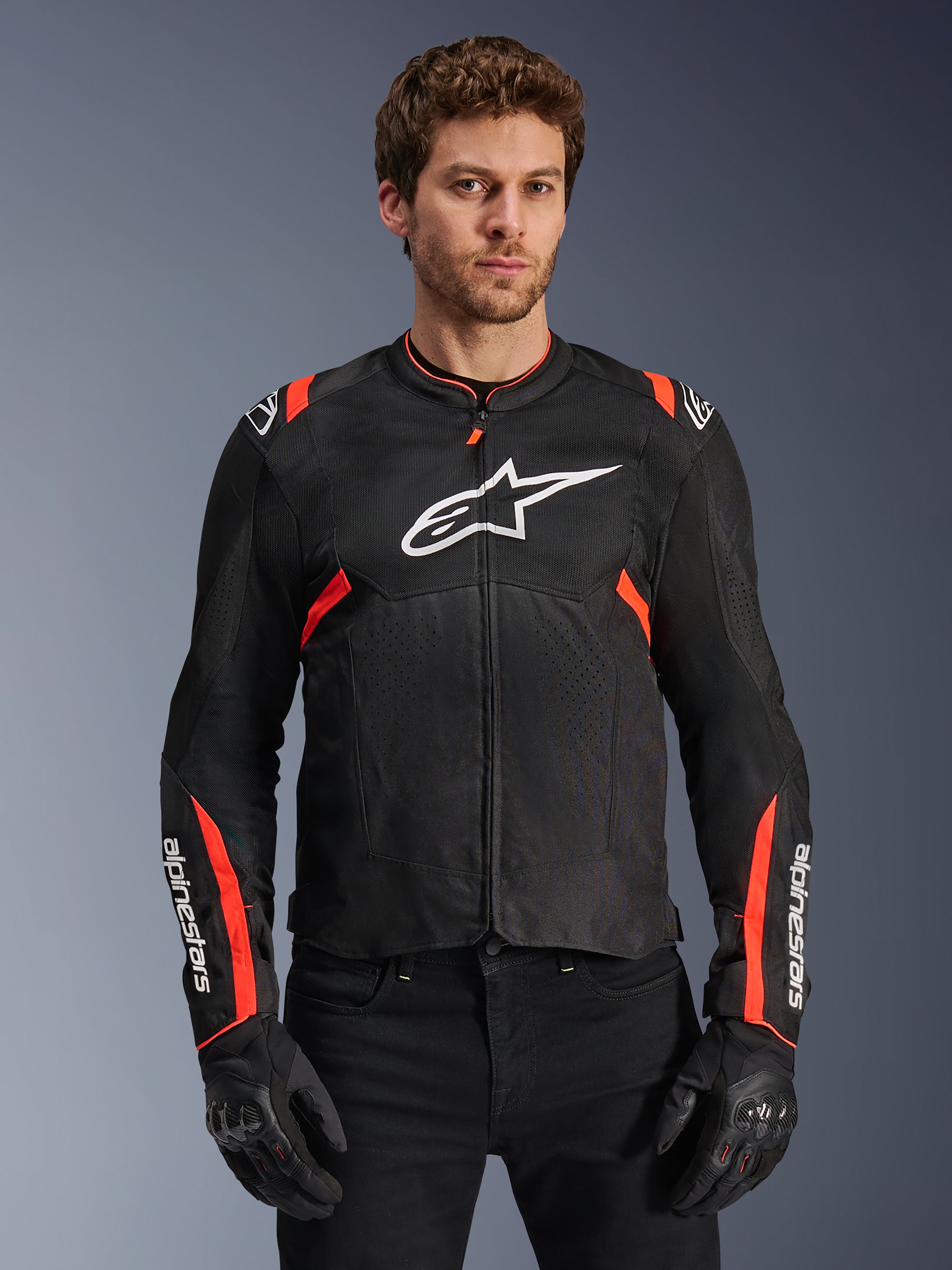 Veste Alpinestars T-Sps Air V2, veste de moto noire et rouge fluo, grand logo Astars blanc sur la poitrine, construction en mesh technique texturé pour la circulation de l'air, portée par un mannequin avec des gants de moto noirs, design coupe sport avec des accents rouges sur les épaules et les manches